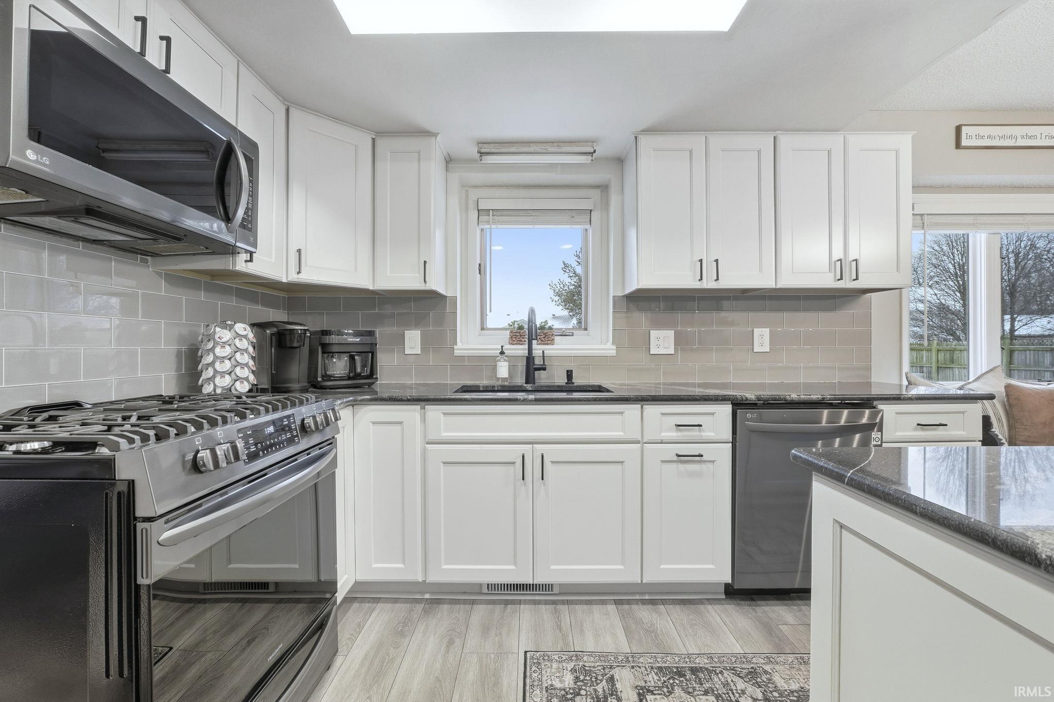 Kitchen with stainless steel appliances, dark stone counters, white cabinetry, and light wood-type flooring