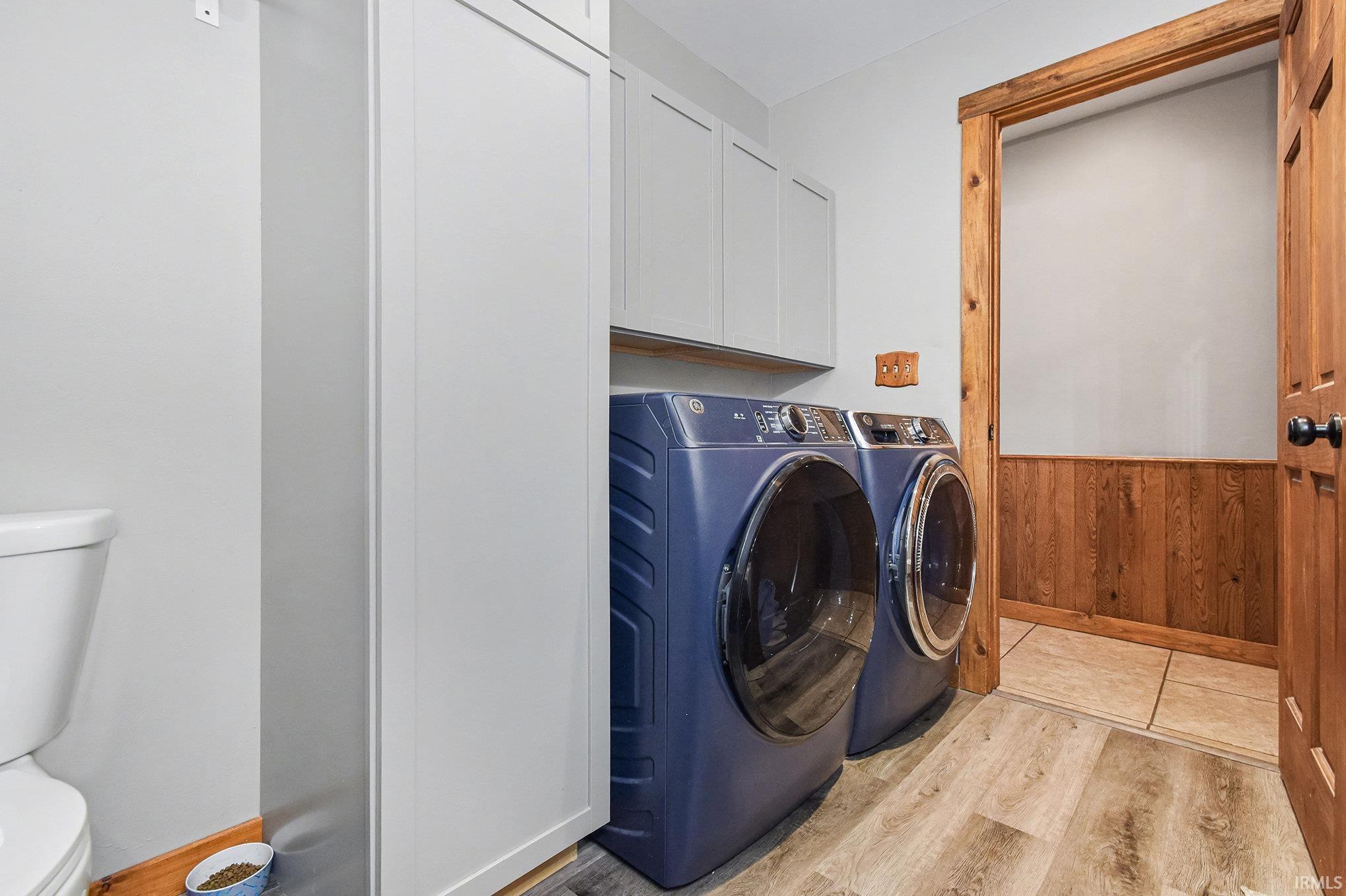 Washroom with light wood-type flooring, wainscoting, wooden walls, and washer and dryer