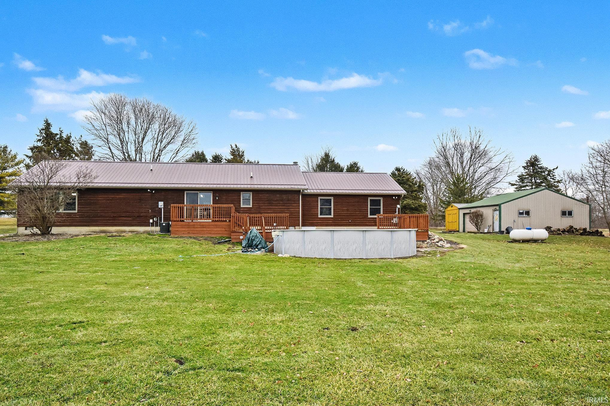 Rear view of house with a lawn, an outdoor pool, a wooden deck, and a metal roof