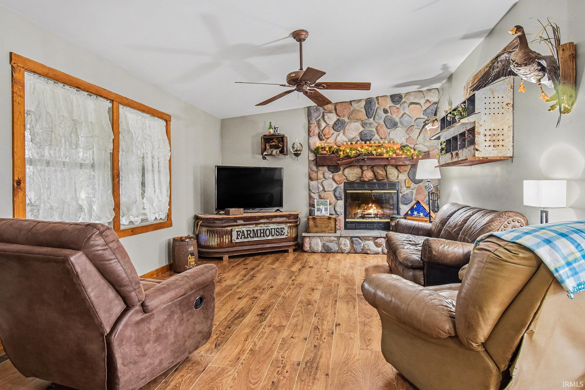 Living room with a stone fireplace, hardwood / wood-style flooring, ceiling fan, and lofted ceiling