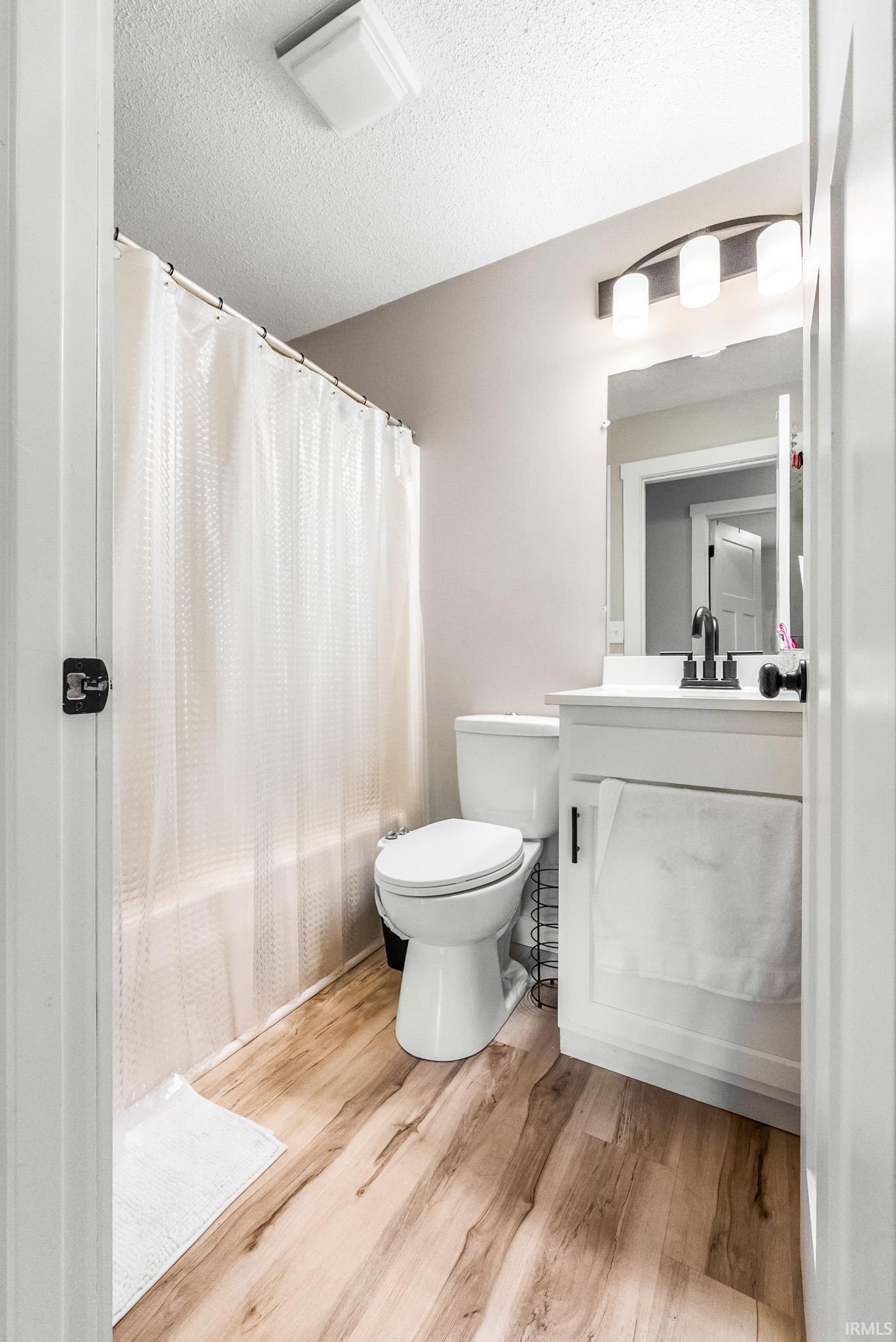 Bathroom with vanity, a textured ceiling, light wood-style flooring, and shower / tub combo with curtain
