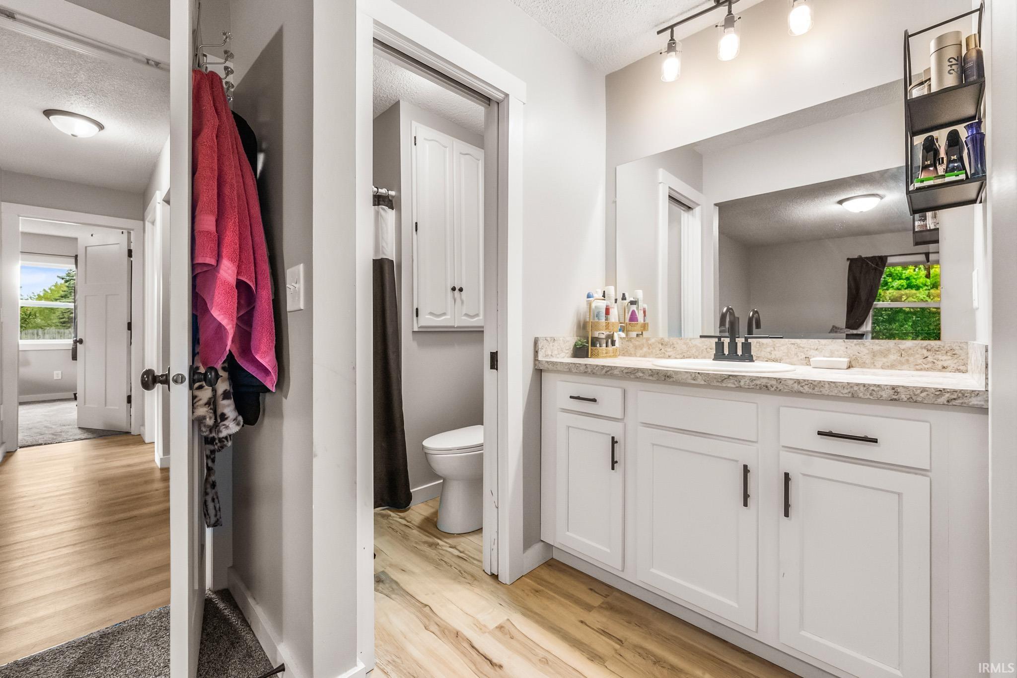 Full bathroom featuring healthy amount of natural light, vanity, a textured ceiling, and light wood-style flooring