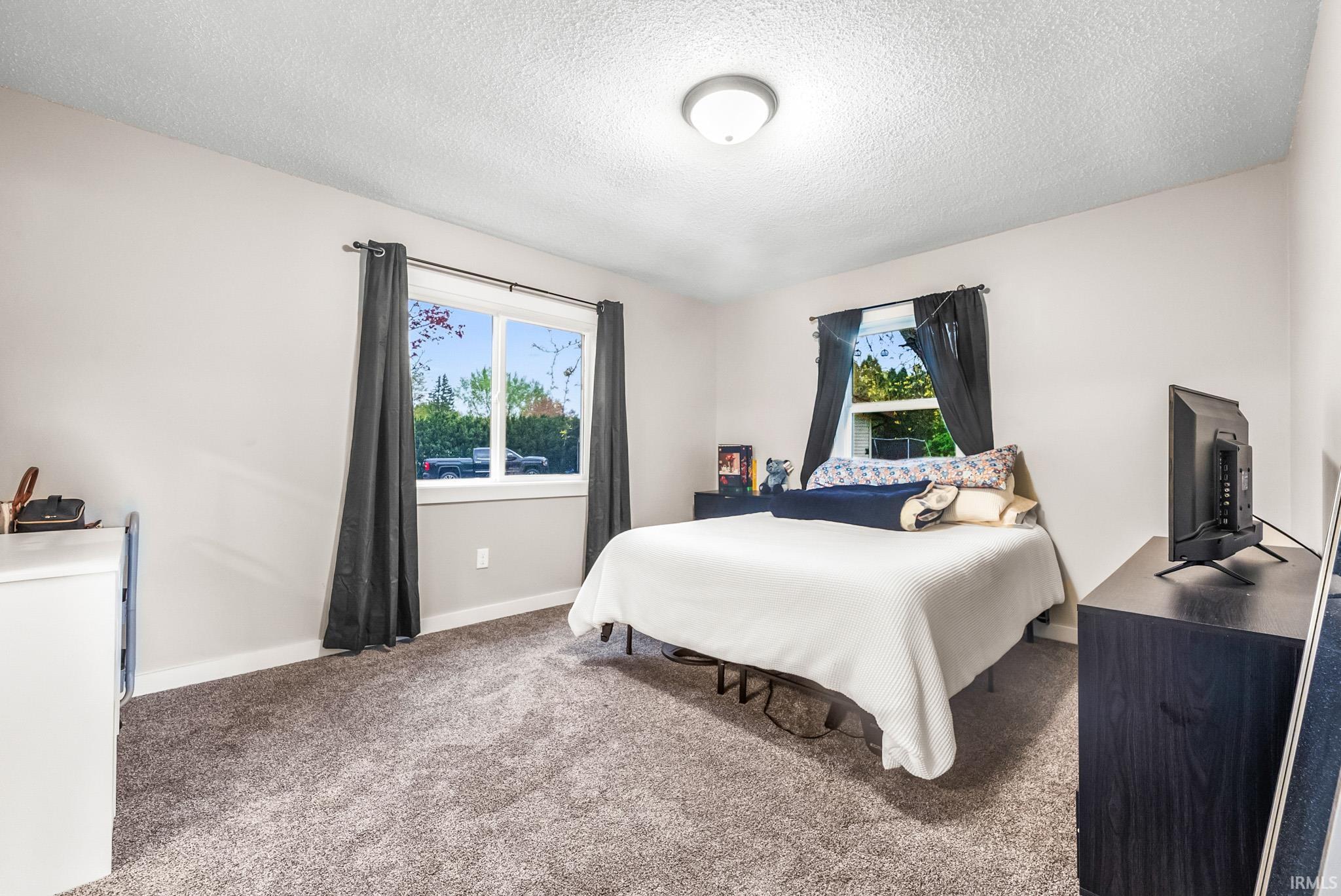 Carpeted bedroom featuring multiple windows and a textured ceiling