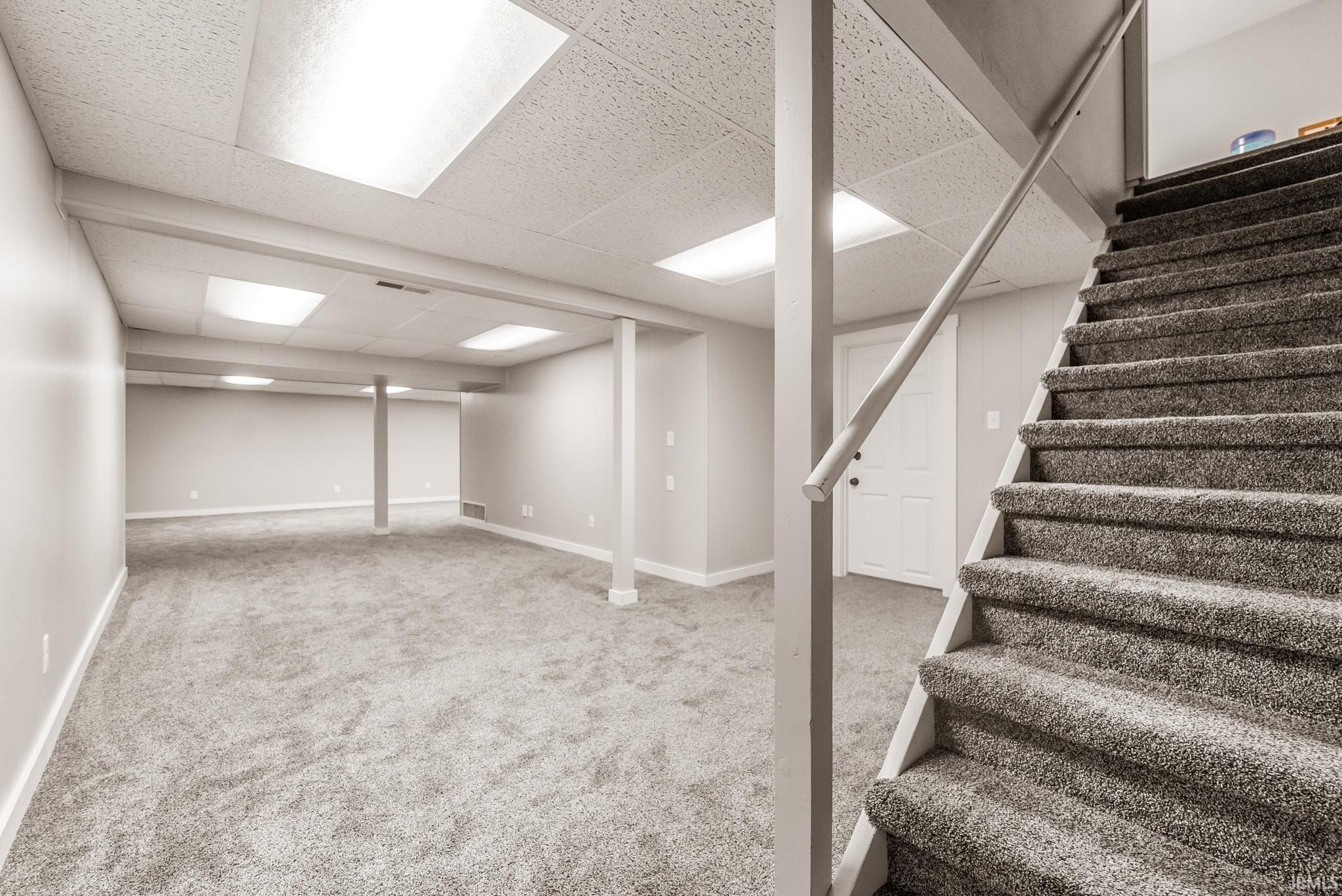 Finished basement with light colored carpet, a drop ceiling, and stairway