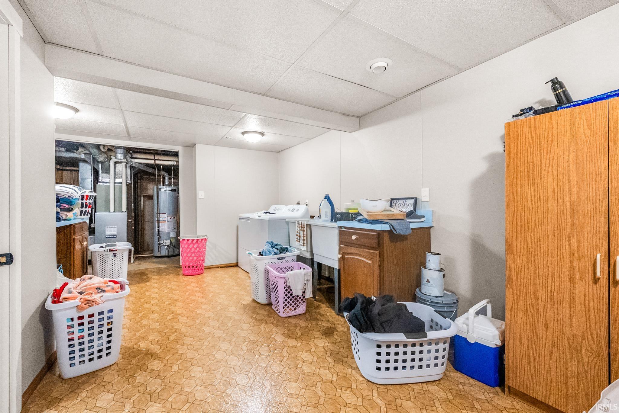 Finished below grade area with light flooring, a drop ceiling, separate washer and dryer, gas water heater, and heating unit
