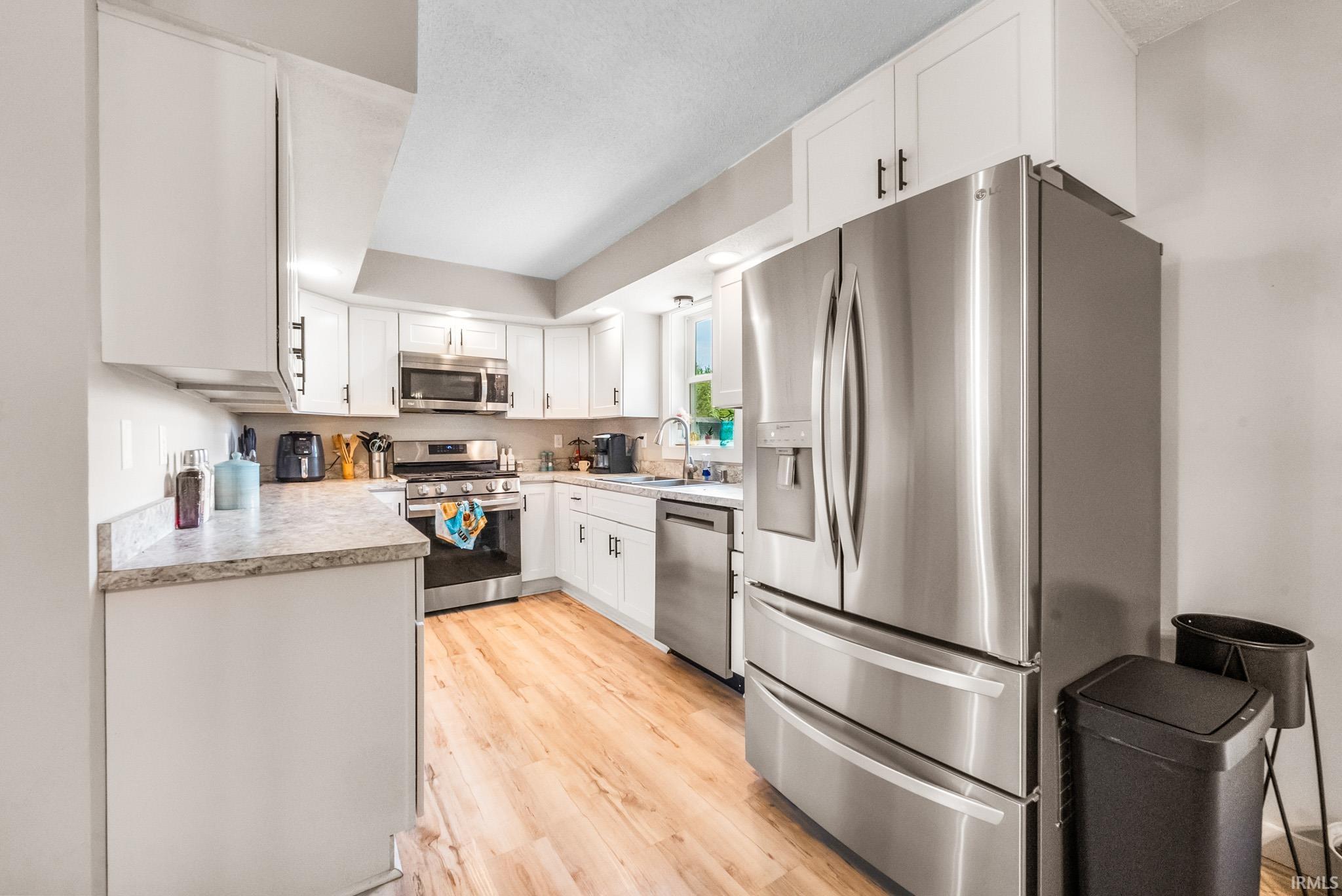 Kitchen featuring stainless steel appliances, light countertops, white cabinets, and light wood-style flooring