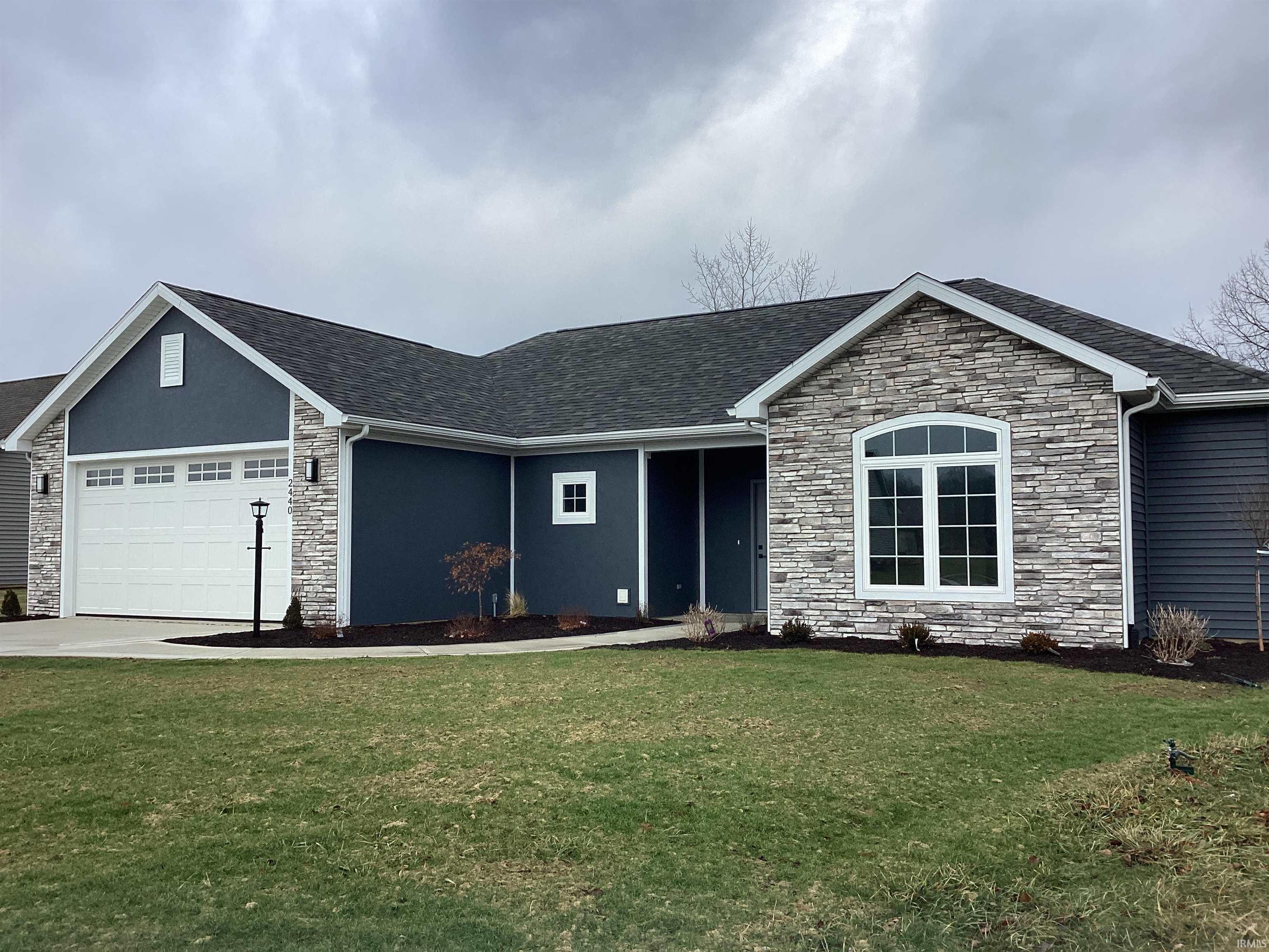 Ranch-style house featuring stone siding, a front lawn, and a garage