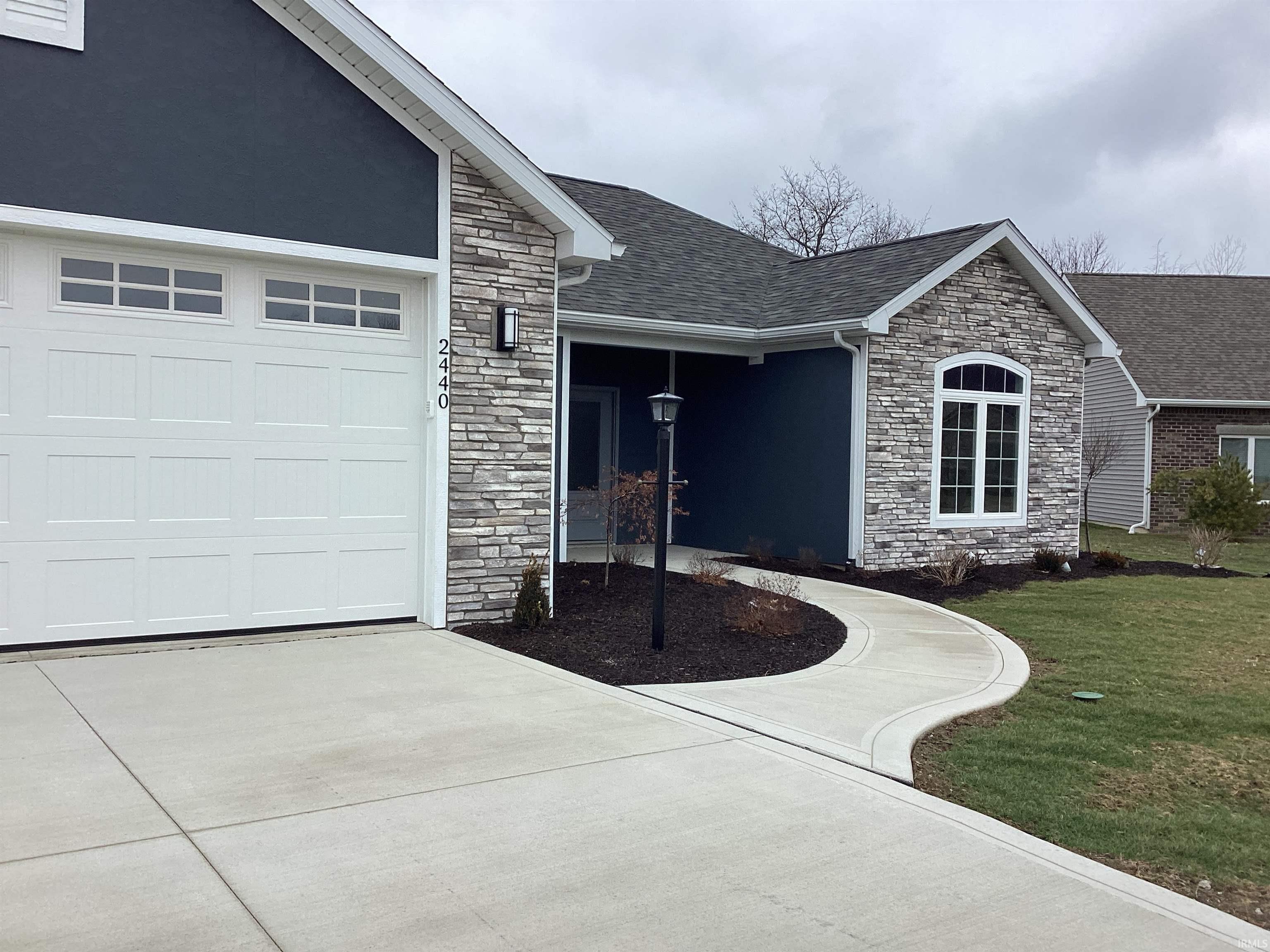 Property entrance featuring stone siding, a shingled roof, driveway, and a garage