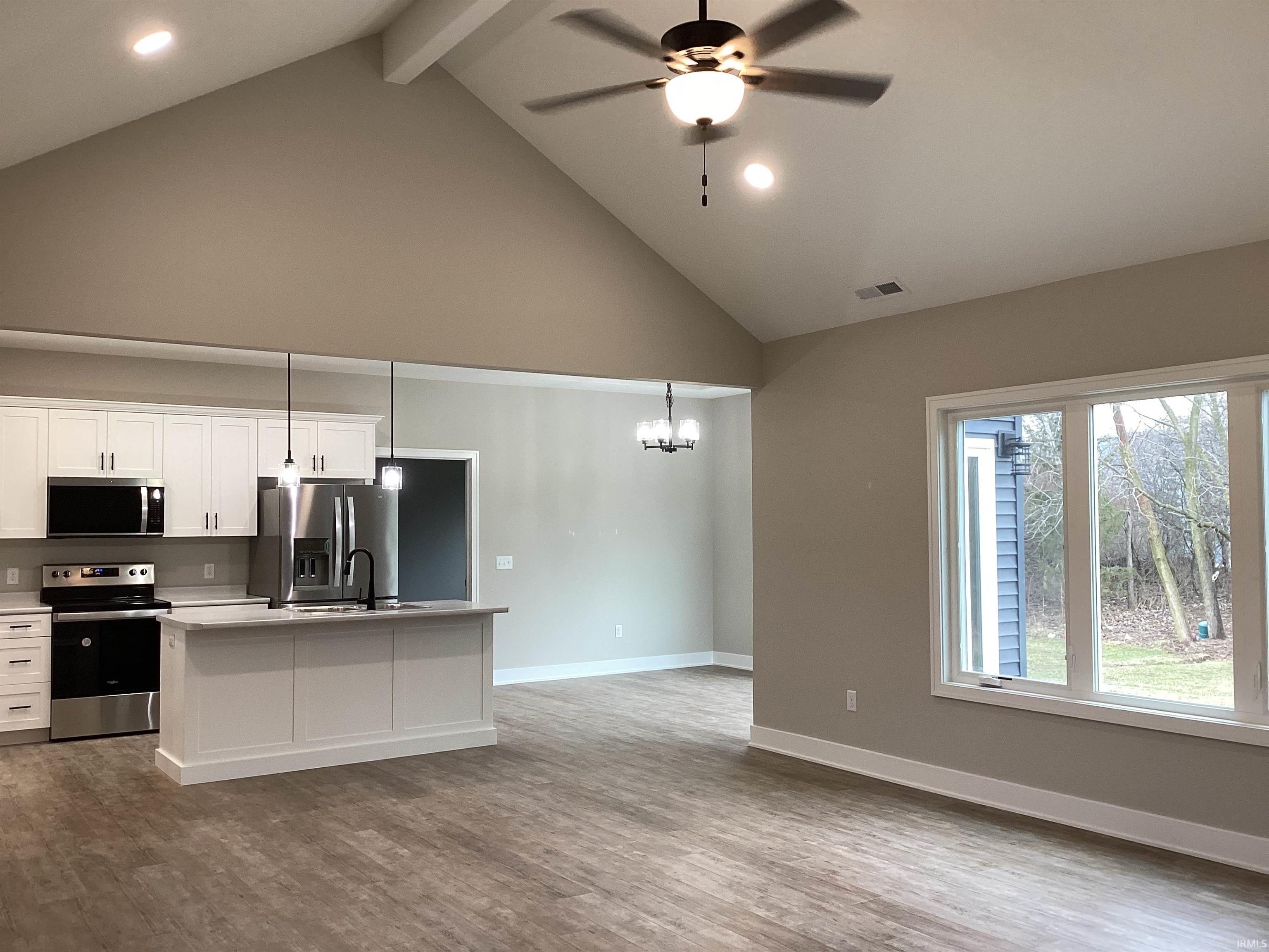 Kitchen featuring appliances with stainless steel finishes, white cabinets, a kitchen island with sink, high vaulted ceiling, and decorative light fixtures
