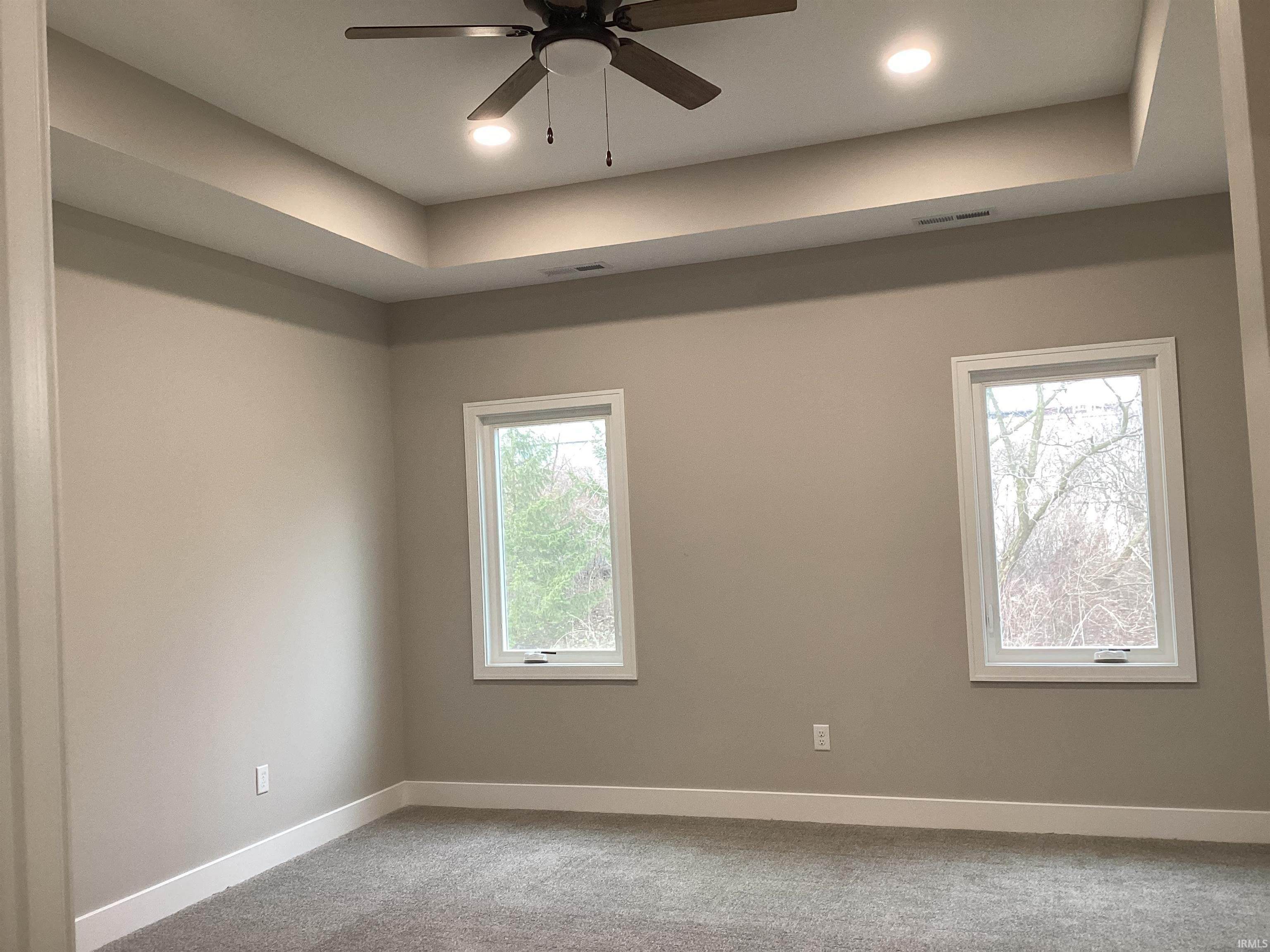 Unfurnished room with a raised ceiling, carpet floors, a ceiling fan, recessed lighting, and healthy amount of natural light