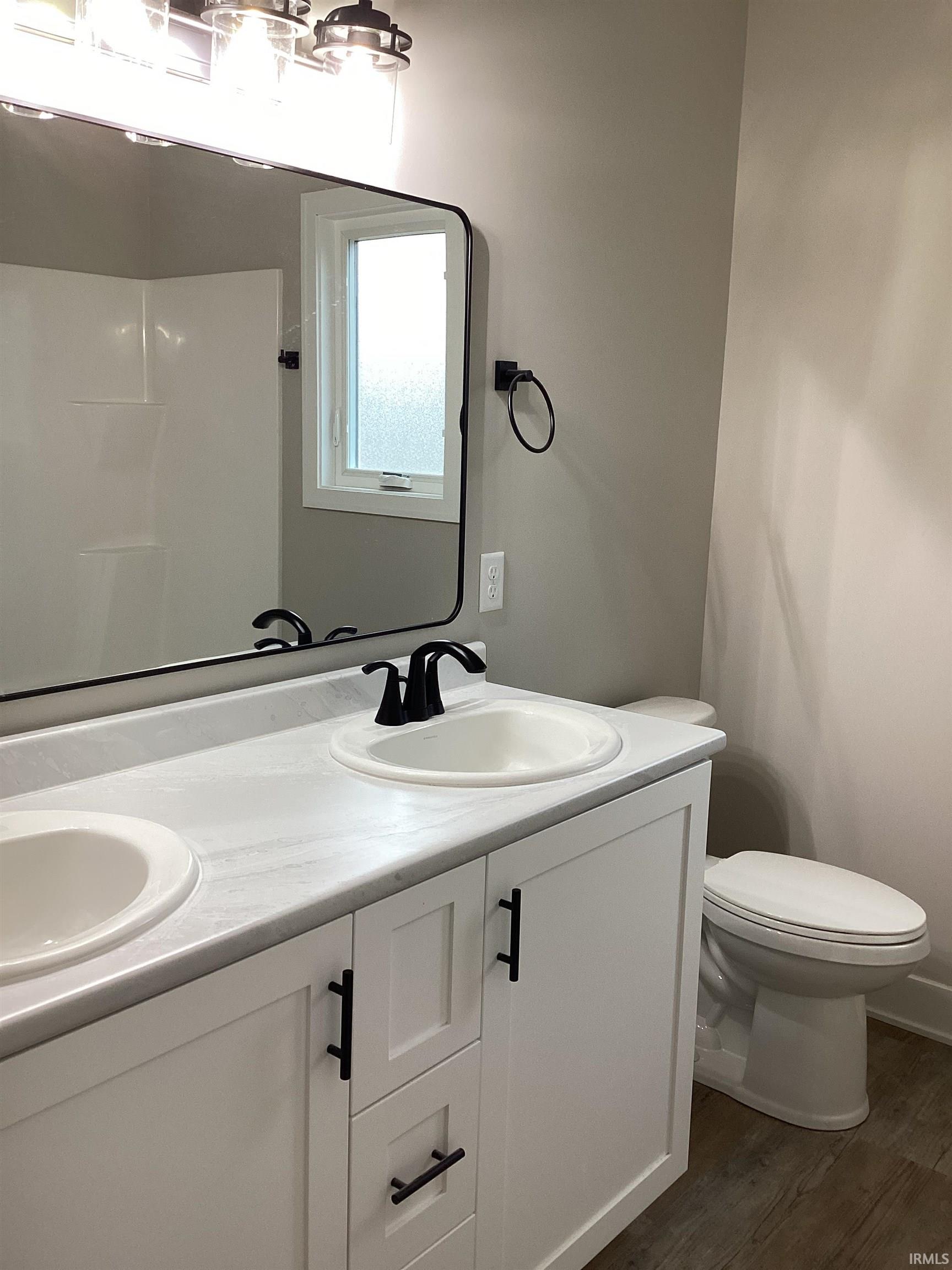 Bathroom with double vanity, dark wood-style flooring, and a shower