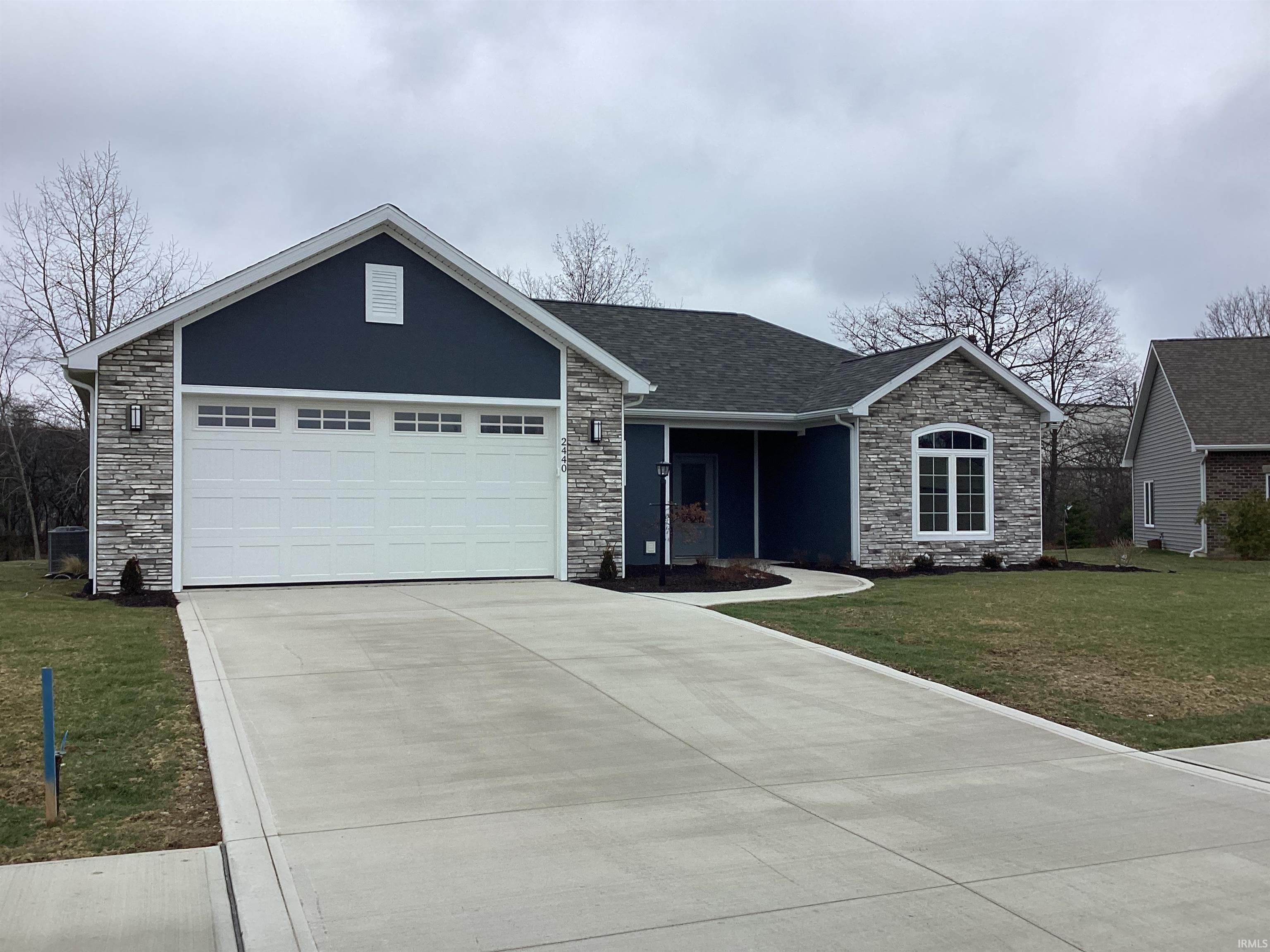 Ranch-style home with stone siding, a front yard, driveway, an attached garage, and a shingled roof