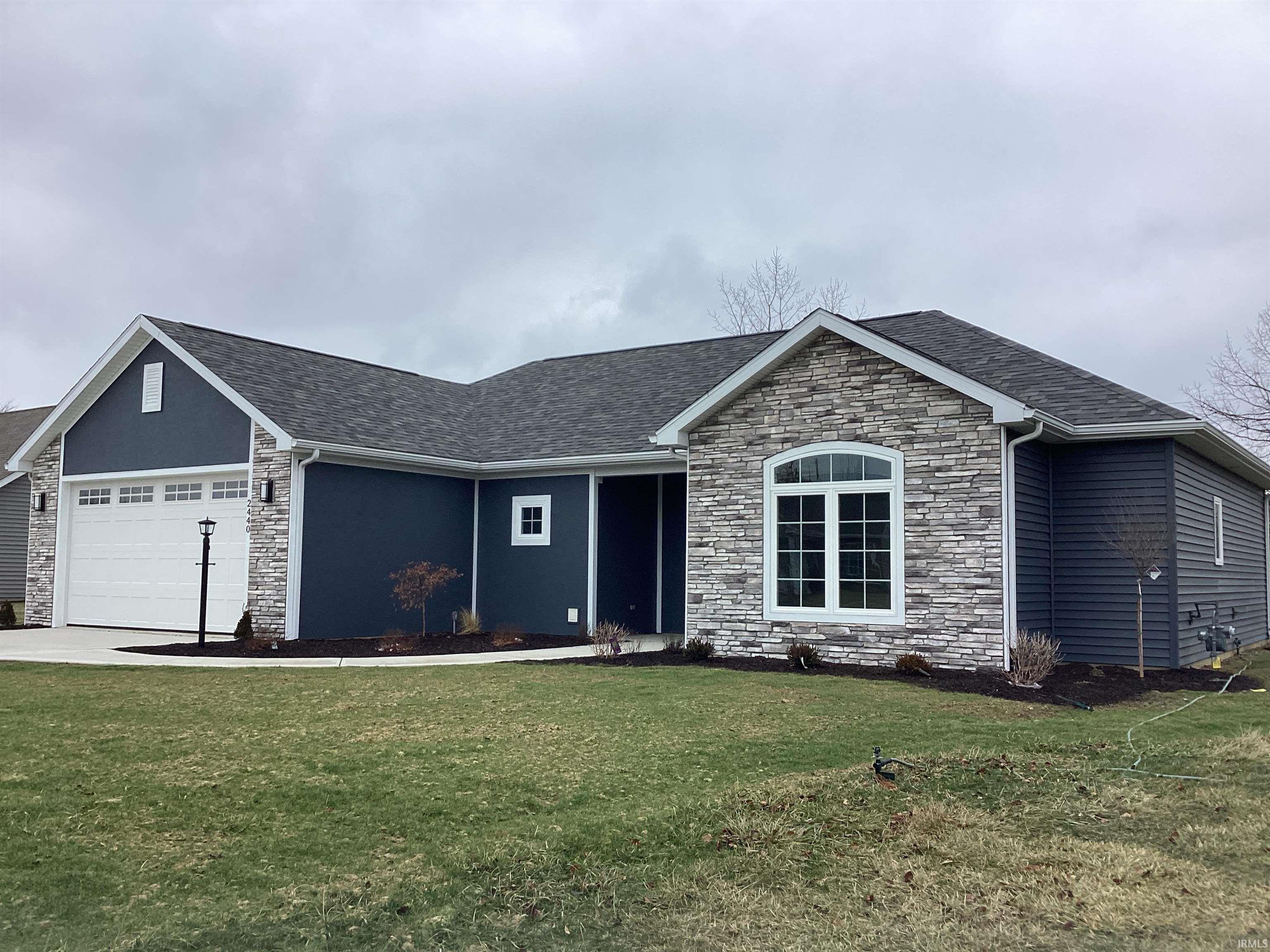 Ranch-style house featuring stone siding, an attached garage, and a front lawn