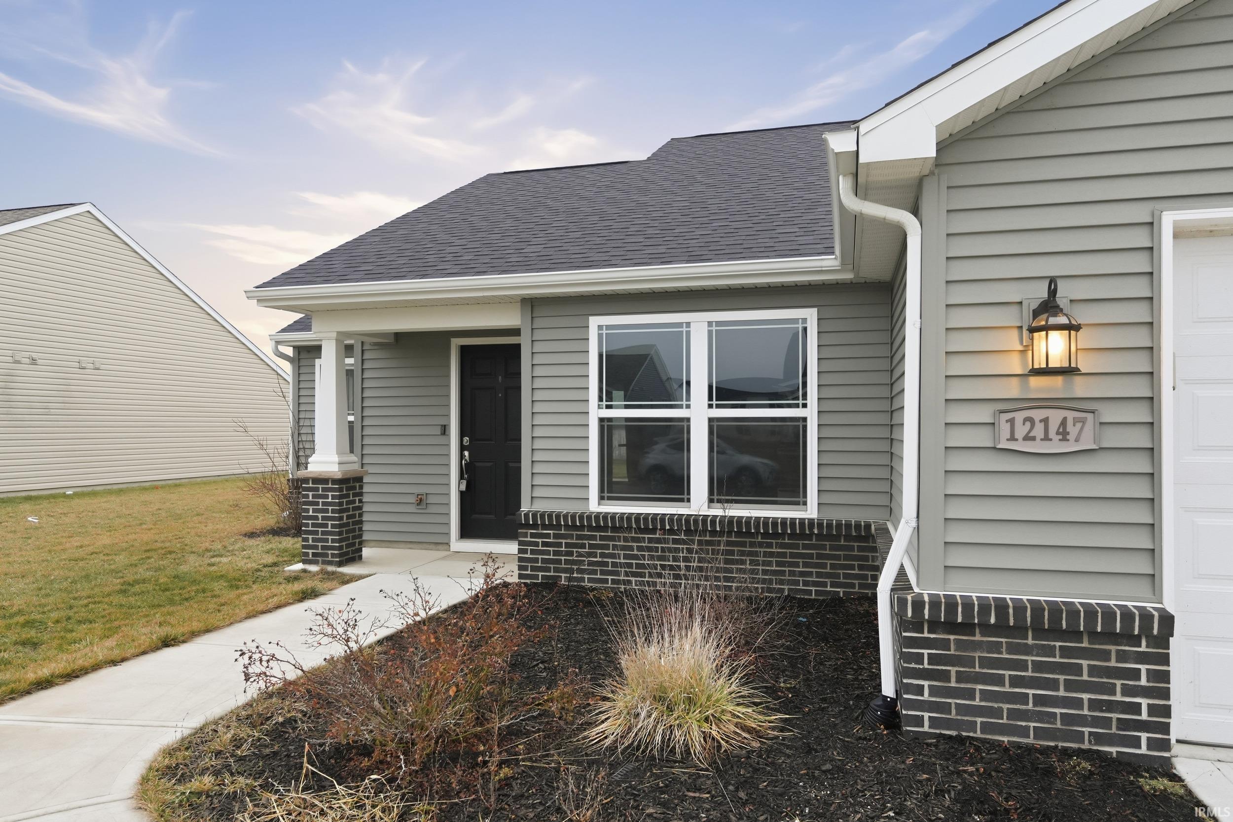 Property entrance featuring roof with shingles, brick siding, a garage, and a lawn