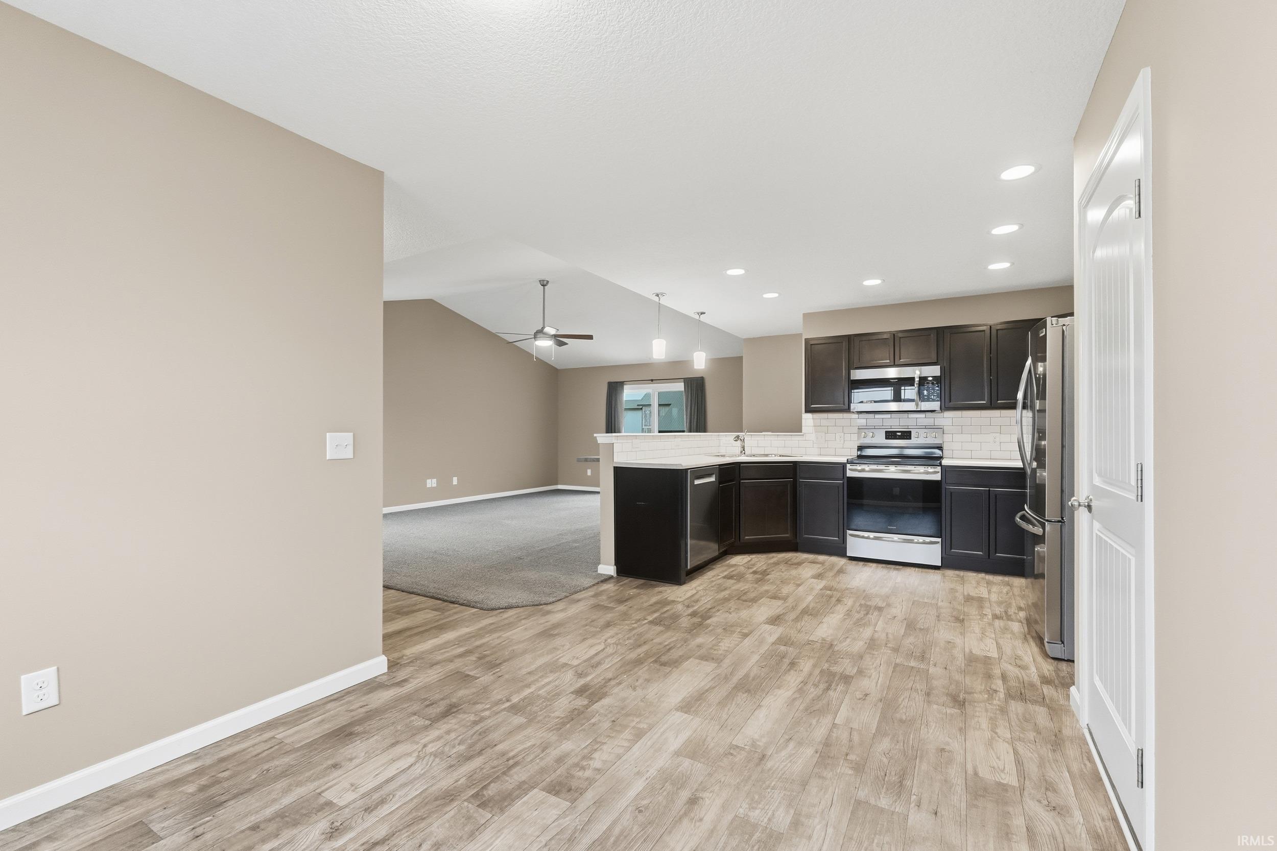 Kitchen with open floor plan, a peninsula, stainless steel appliances, vaulted ceiling, and ceiling fan
