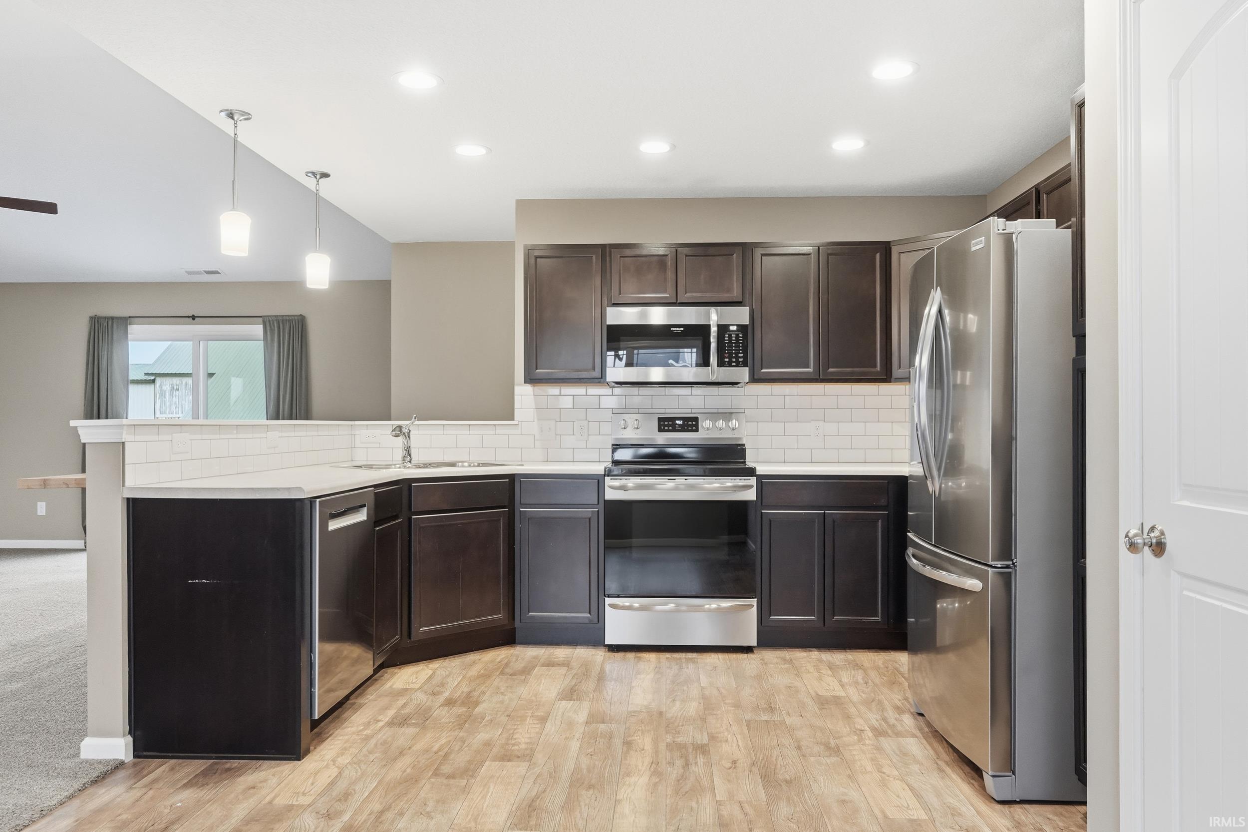 Kitchen with appliances with stainless steel finishes, decorative backsplash, decorative light fixtures, dark brown cabinetry, and a peninsula