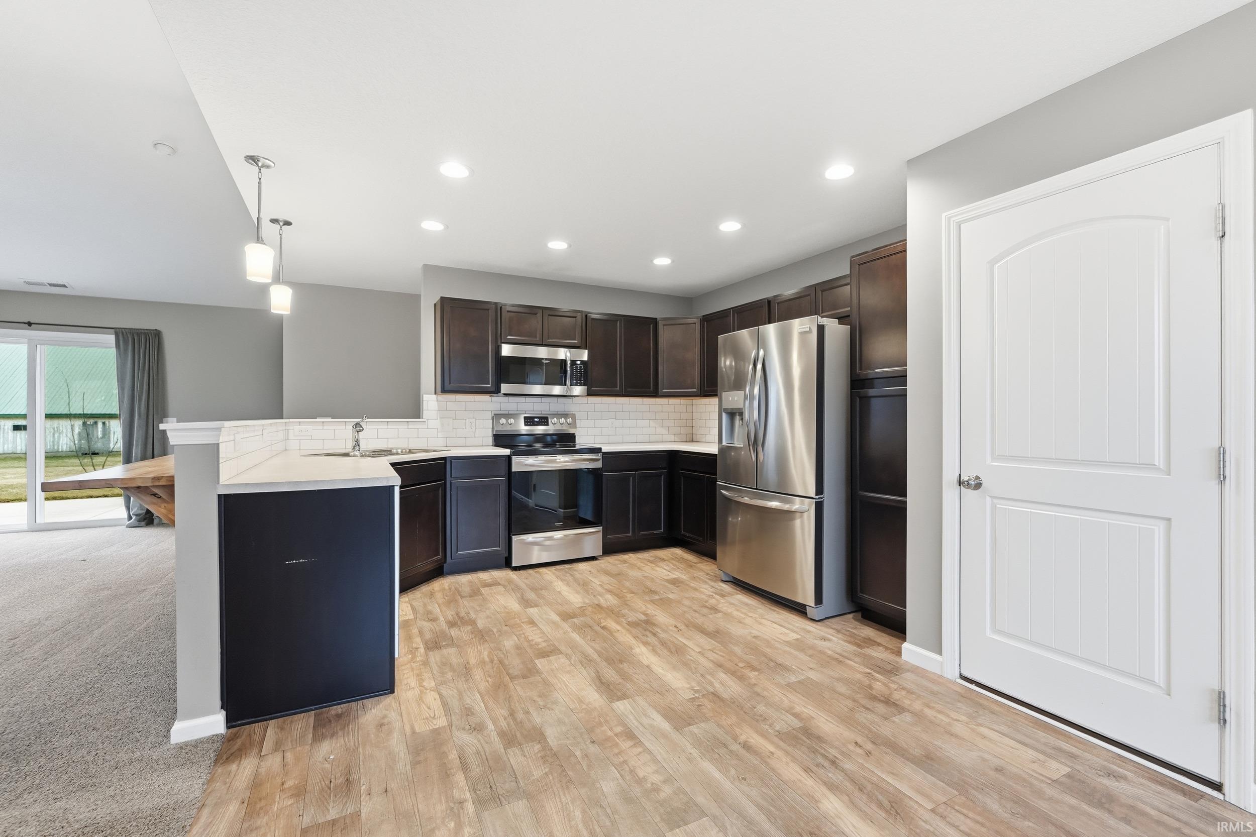 Kitchen featuring stainless steel appliances, dark brown cabinetry, backsplash, hanging light fixtures, and a peninsula