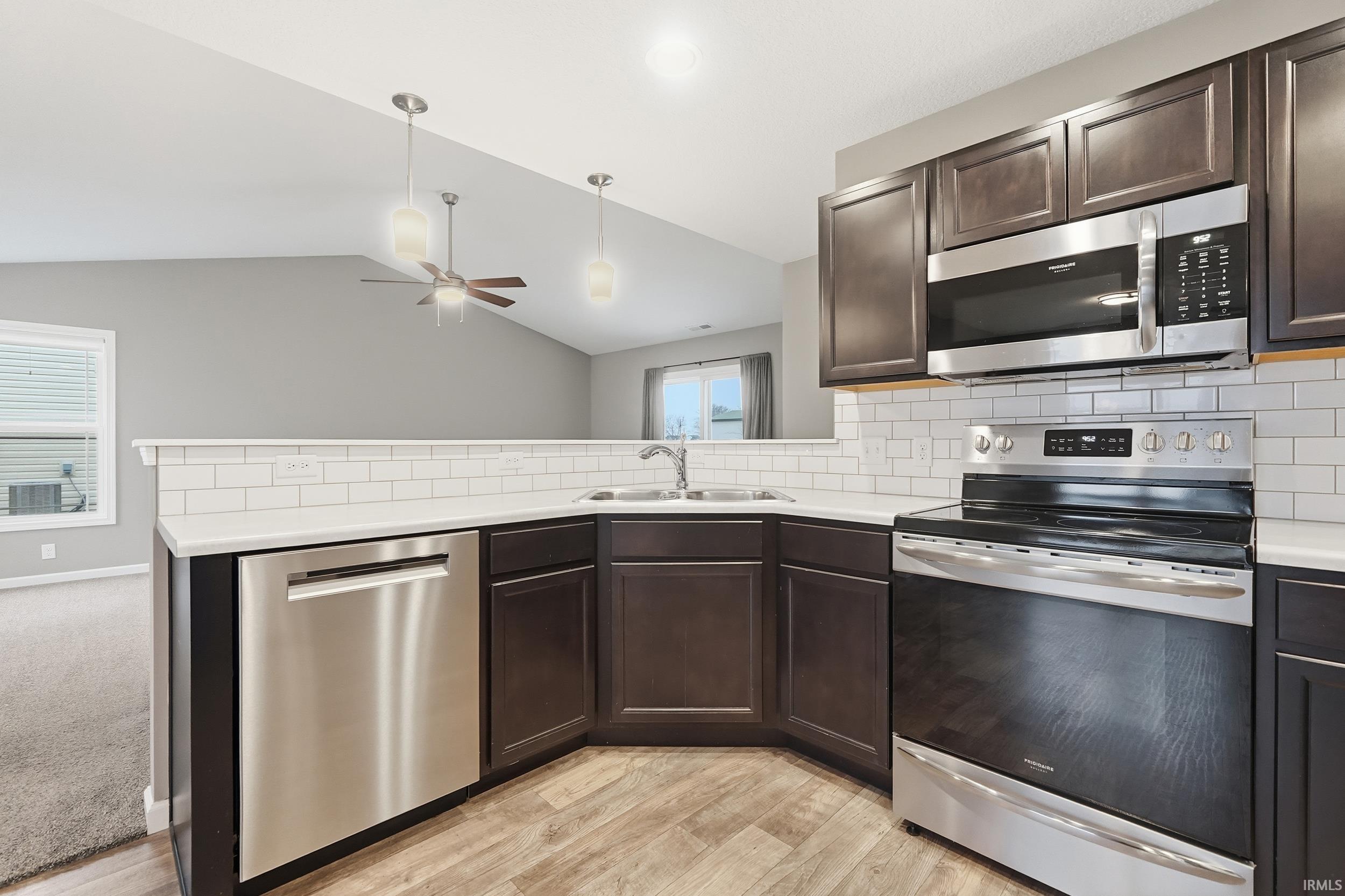 Kitchen featuring appliances with stainless steel finishes, dark brown cabinetry, light countertops, backsplash, and vaulted ceiling