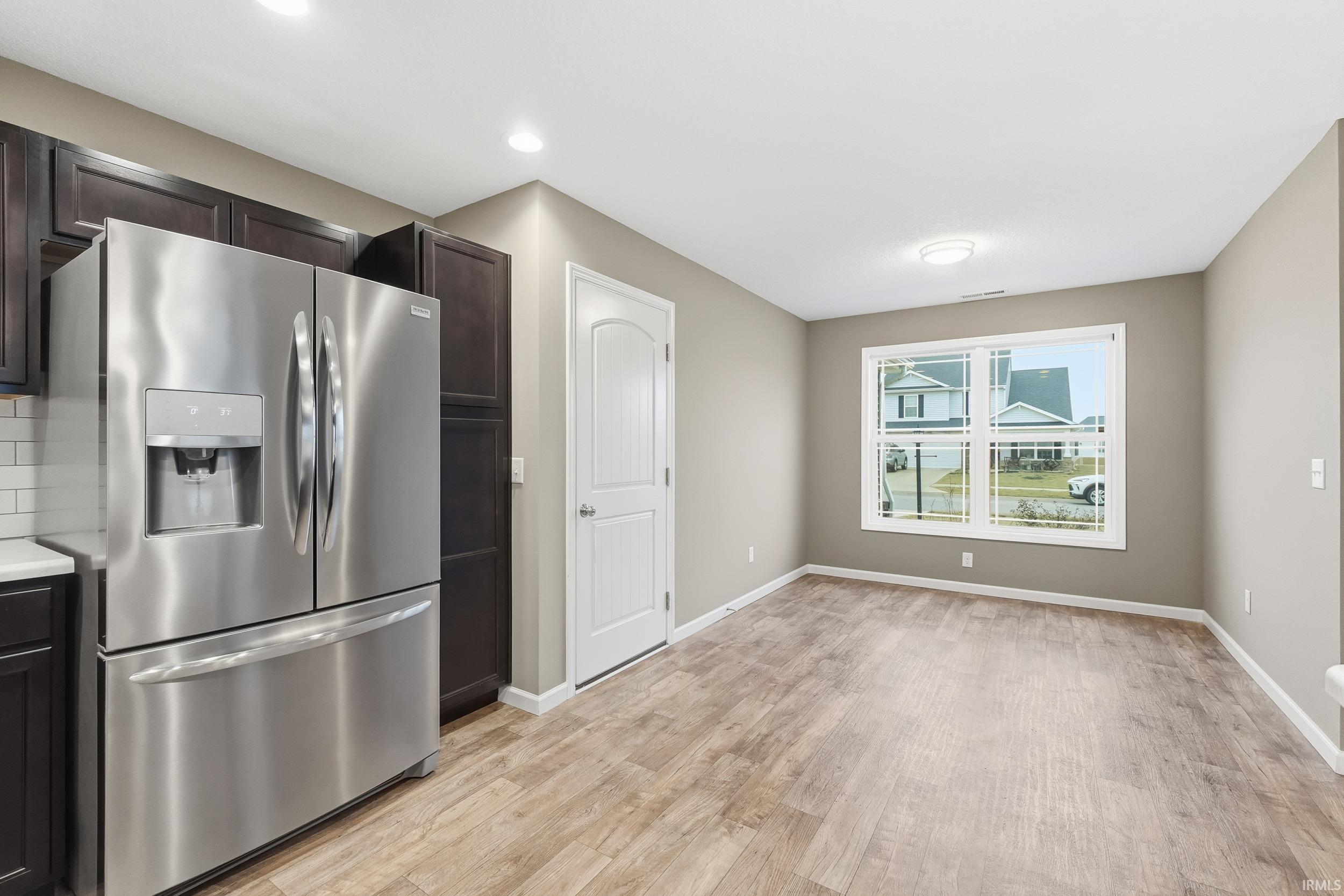 Kitchen featuring stainless steel fridge, light wood-type flooring, dark brown cabinetry, light countertops, and decorative backsplash
