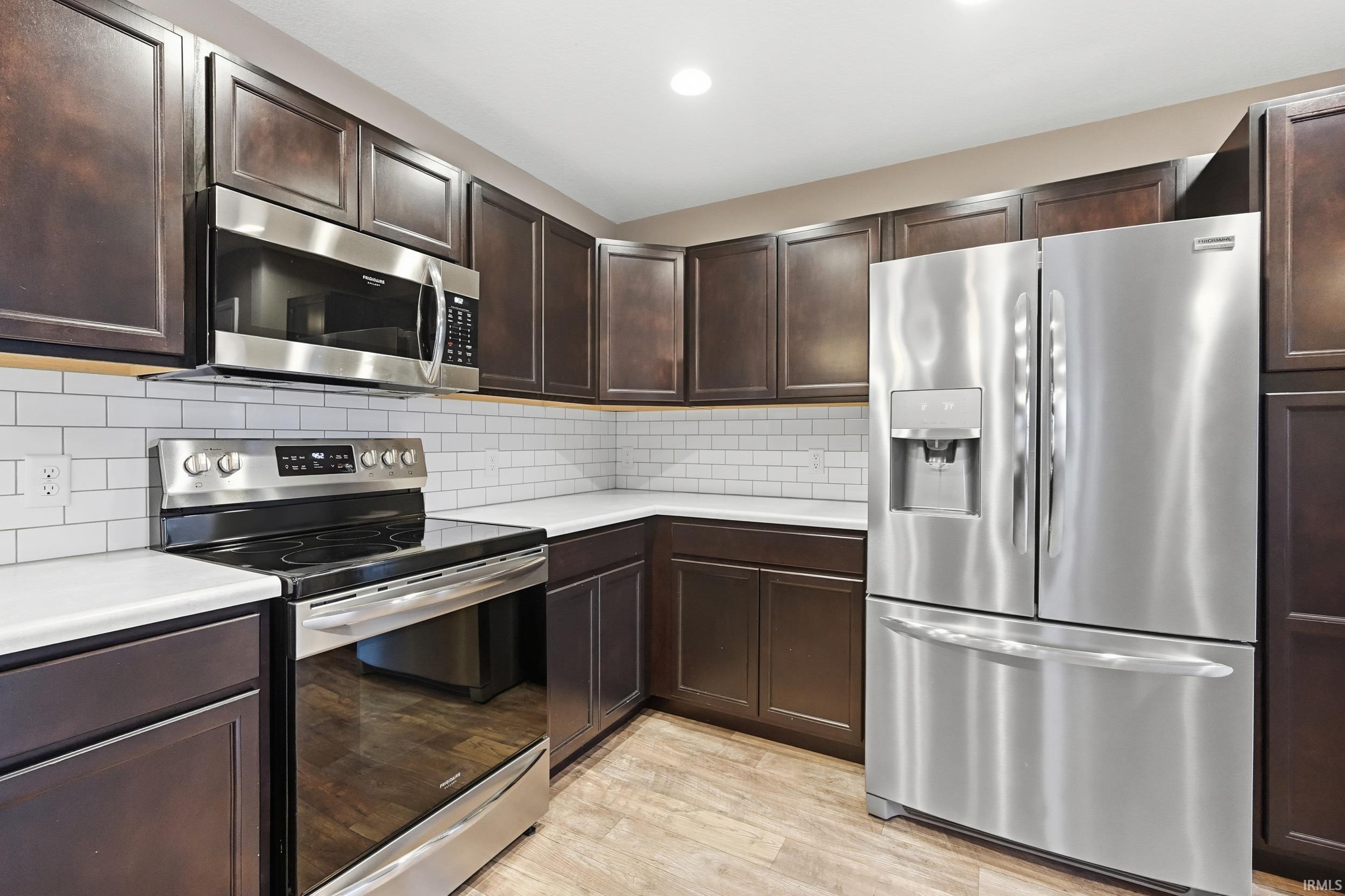 Kitchen with appliances with stainless steel finishes, light countertops, dark brown cabinetry, light wood finished floors, and decorative backsplash