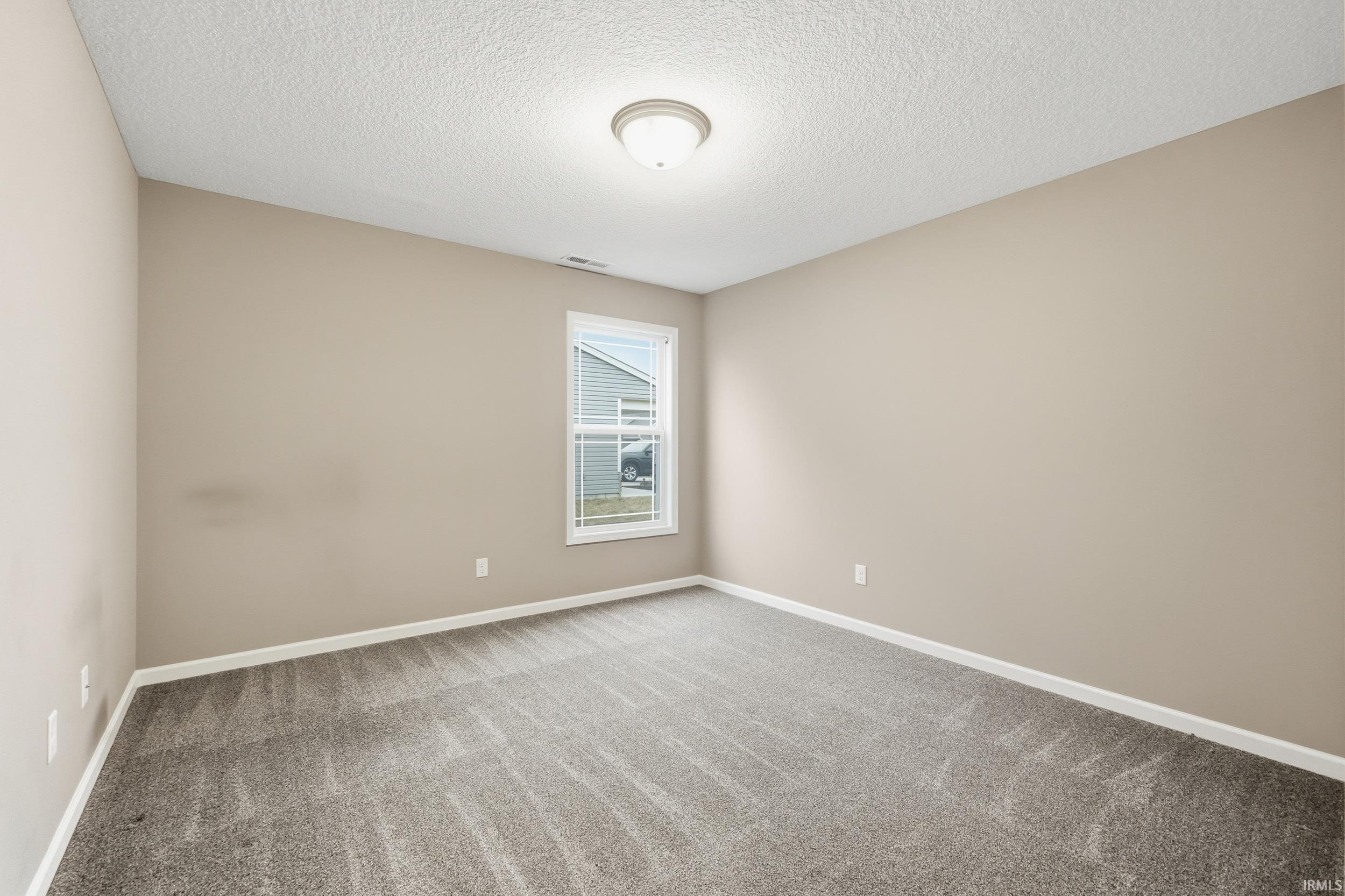 Carpeted empty room featuring a textured ceiling and baseboards