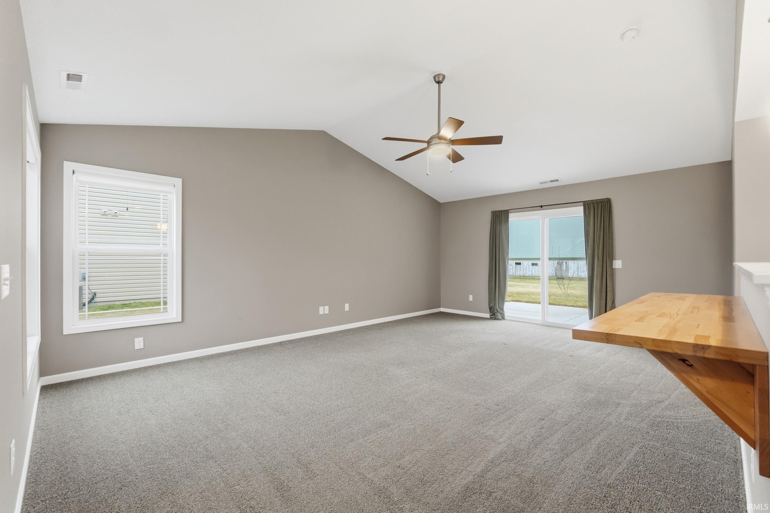 Empty room with vaulted ceiling, light carpet, and ceiling fan