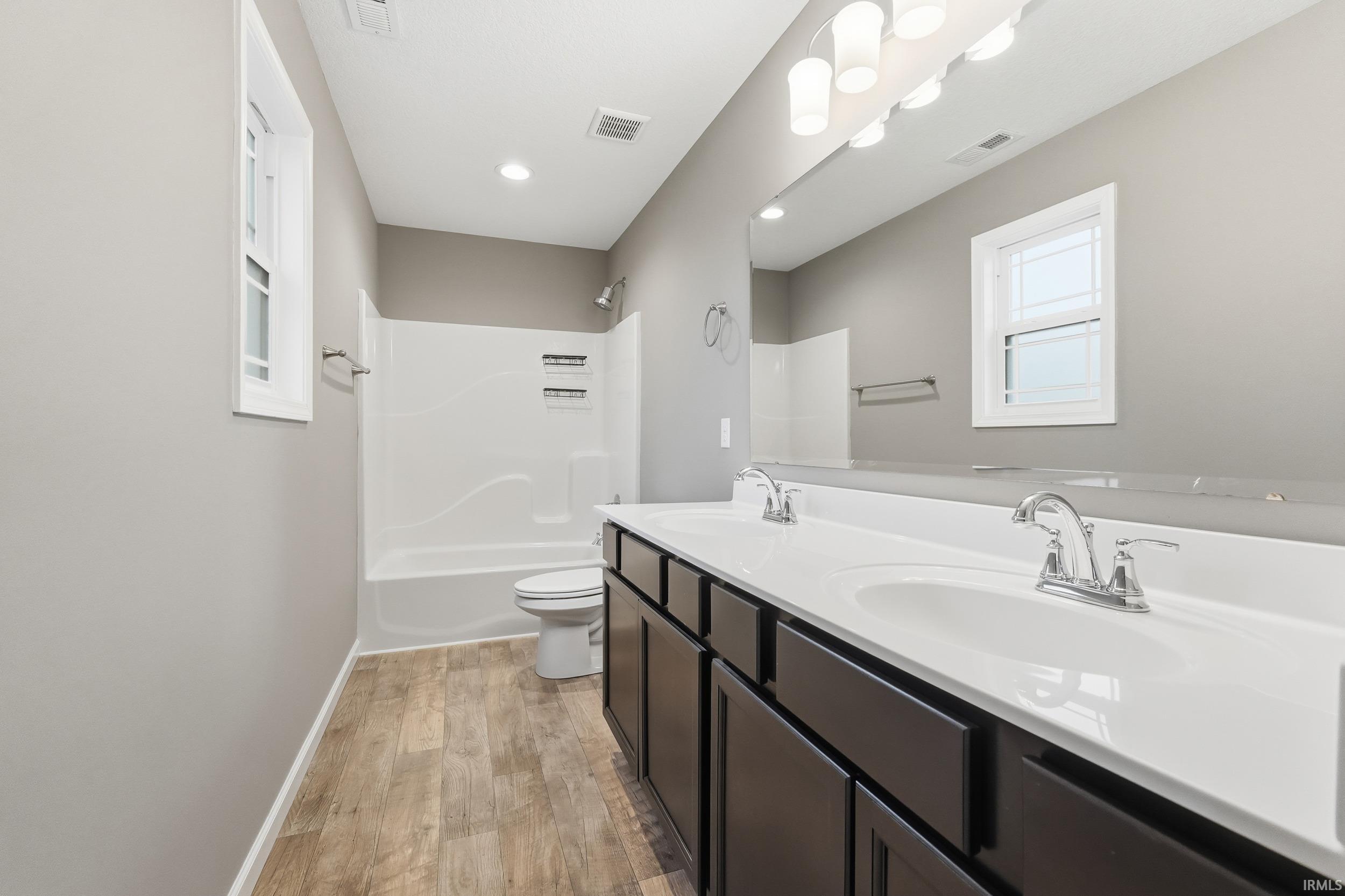 Bathroom featuring double vanity, light wood-type flooring, and shower / washtub combination