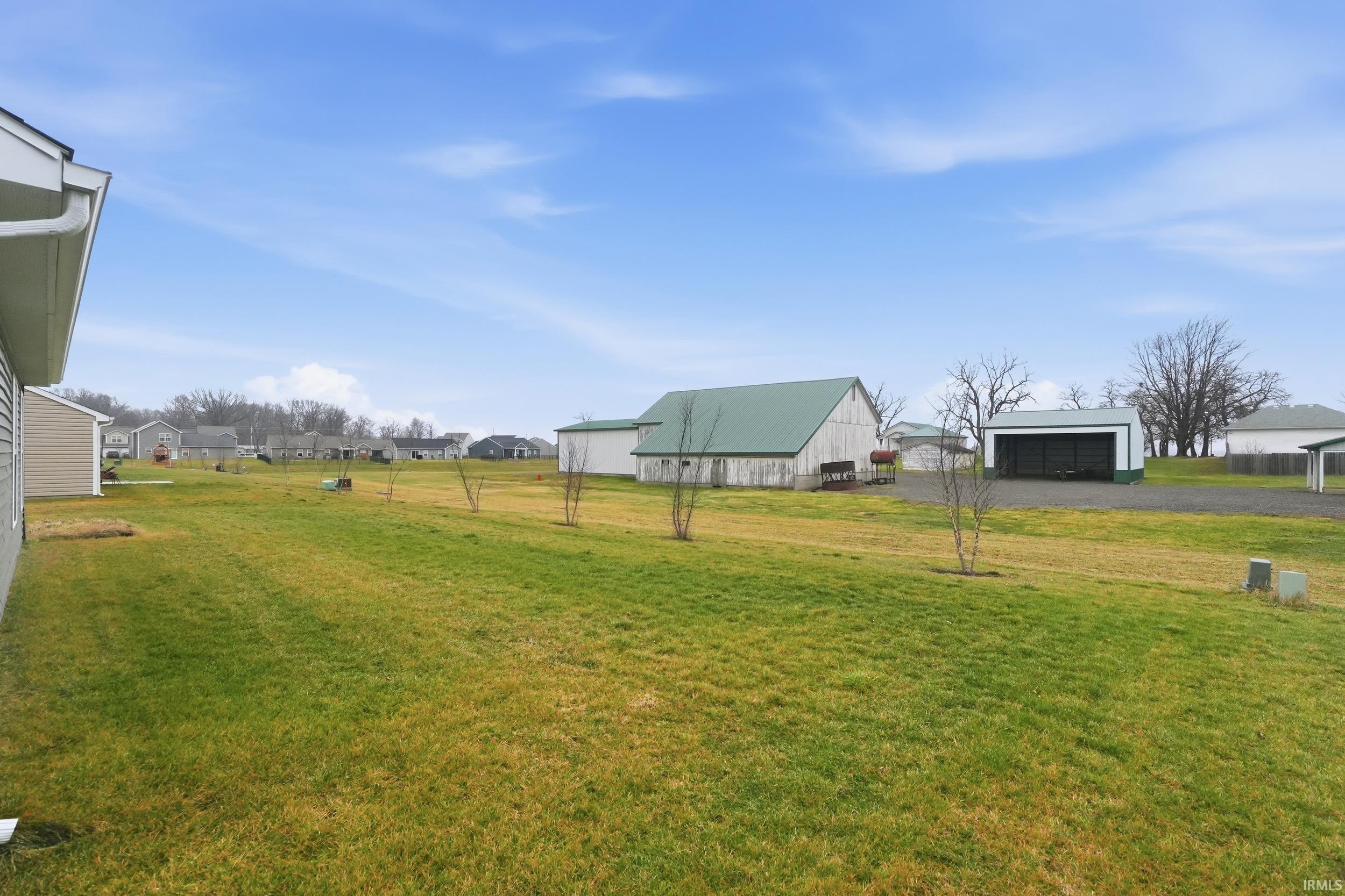 View of grassy yard featuring an outdoor structure, a pole building, a garage, and driveway