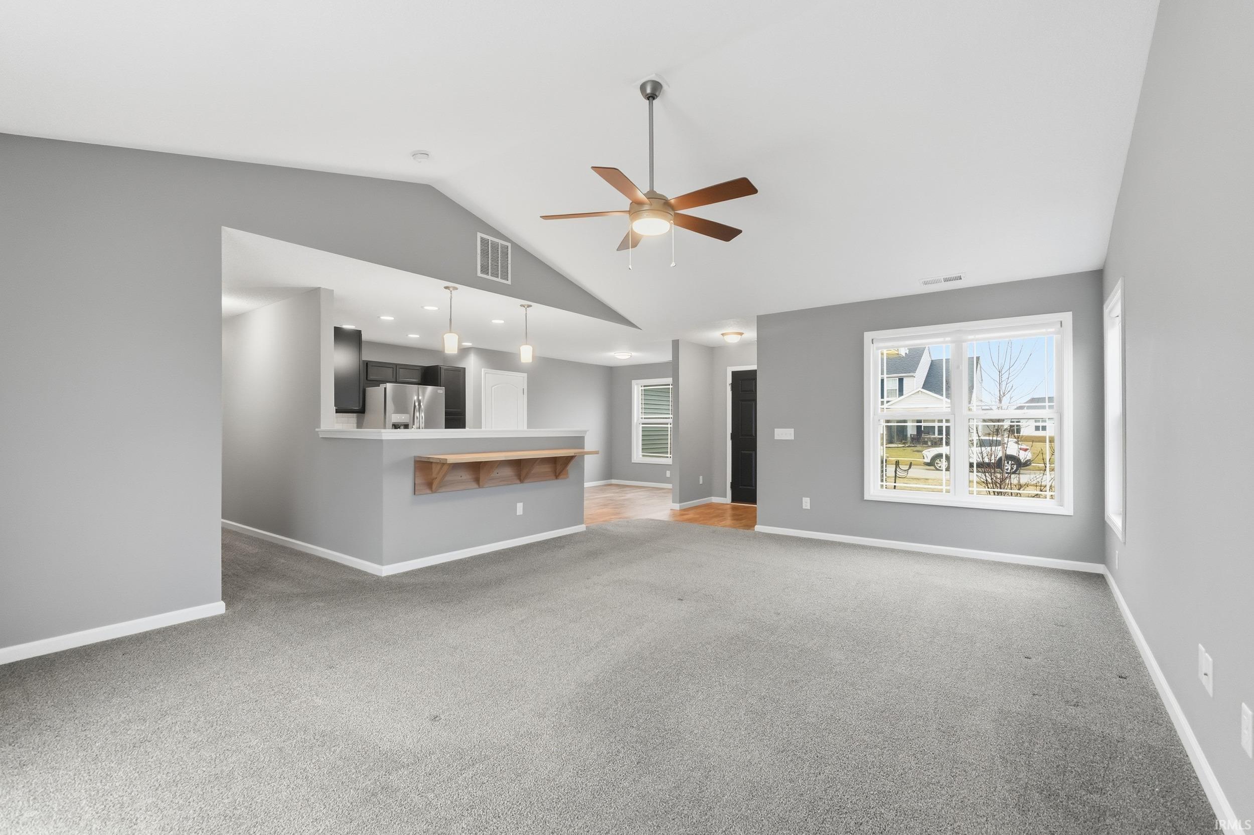 Unfurnished living room featuring light carpet, vaulted ceiling, and ceiling fan