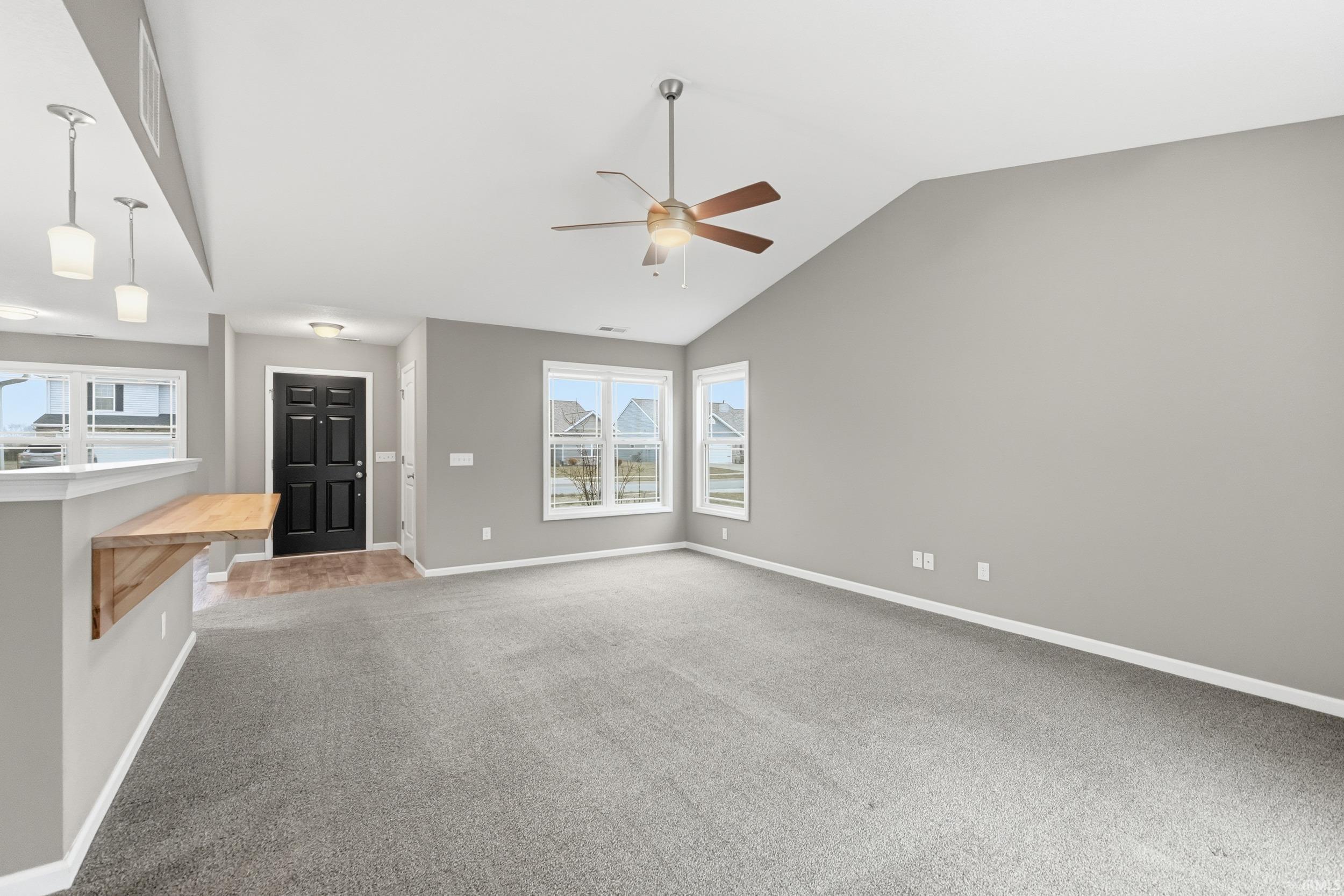 Unfurnished living room featuring light carpet, vaulted ceiling, and ceiling fan