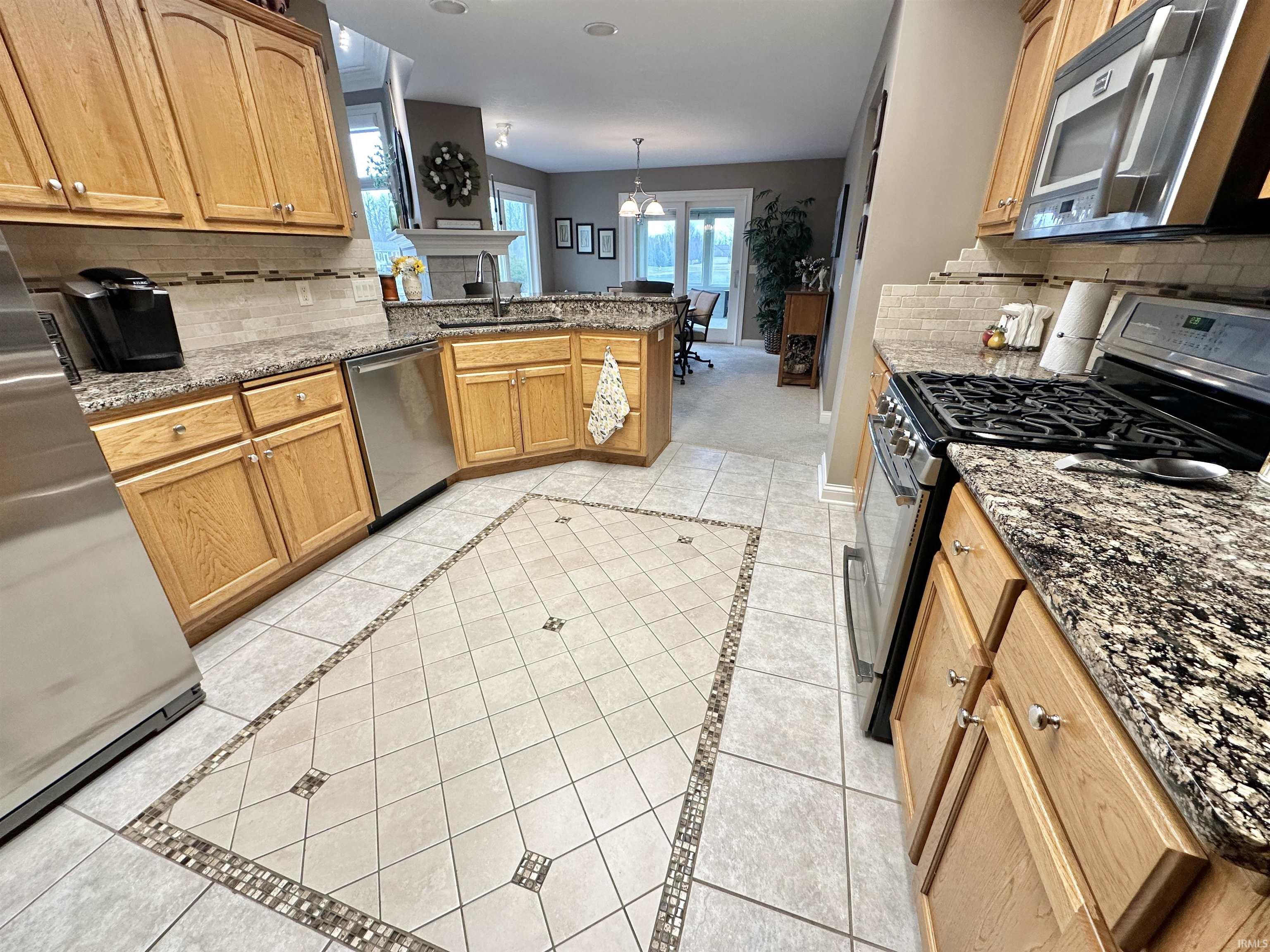 Kitchen with backsplash, stainless steel appliances, dark stone countertops, and inlaid floor details