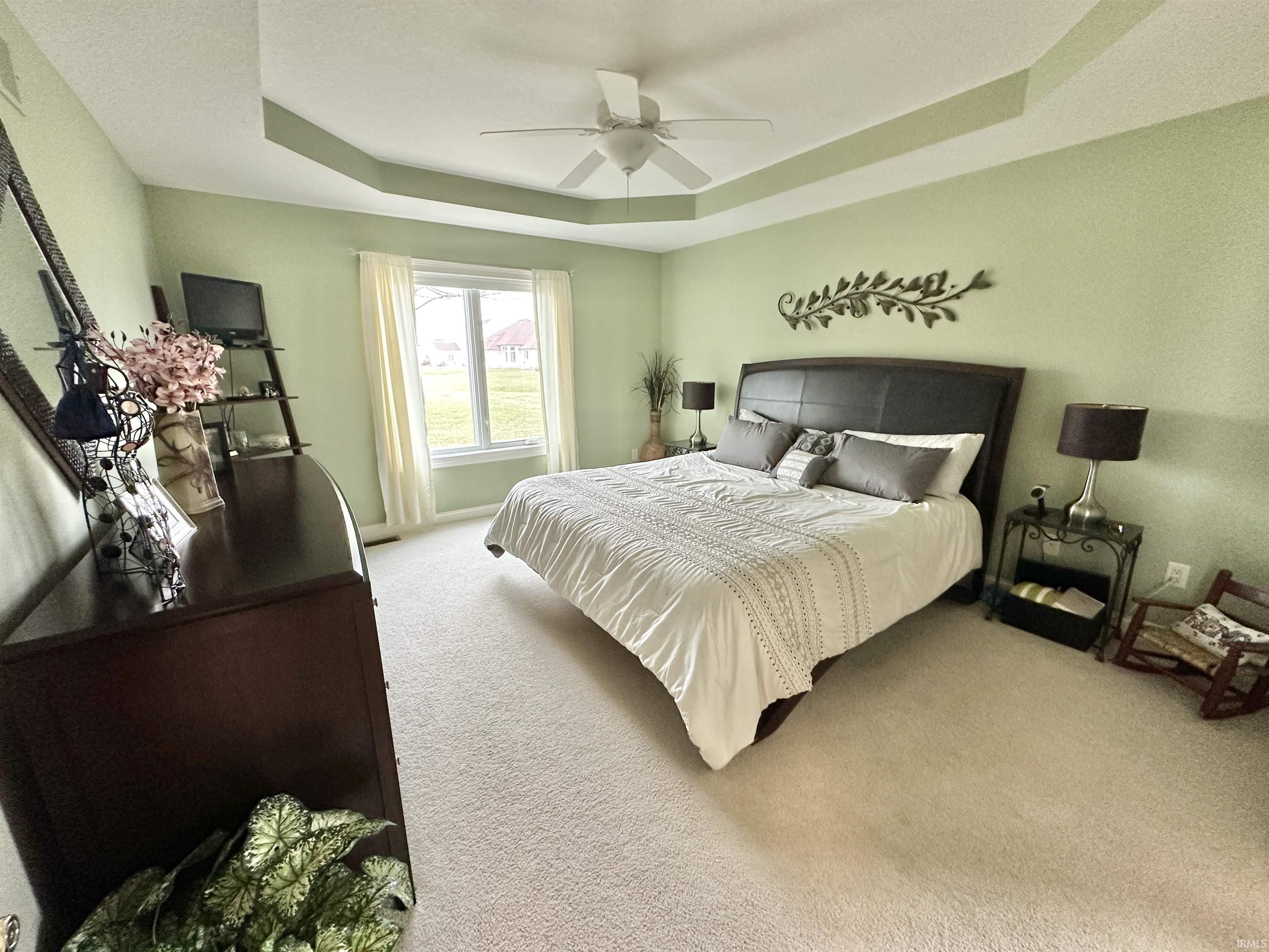 Bedroom featuring a raised ceiling, carpet floors, and a ceiling fan
