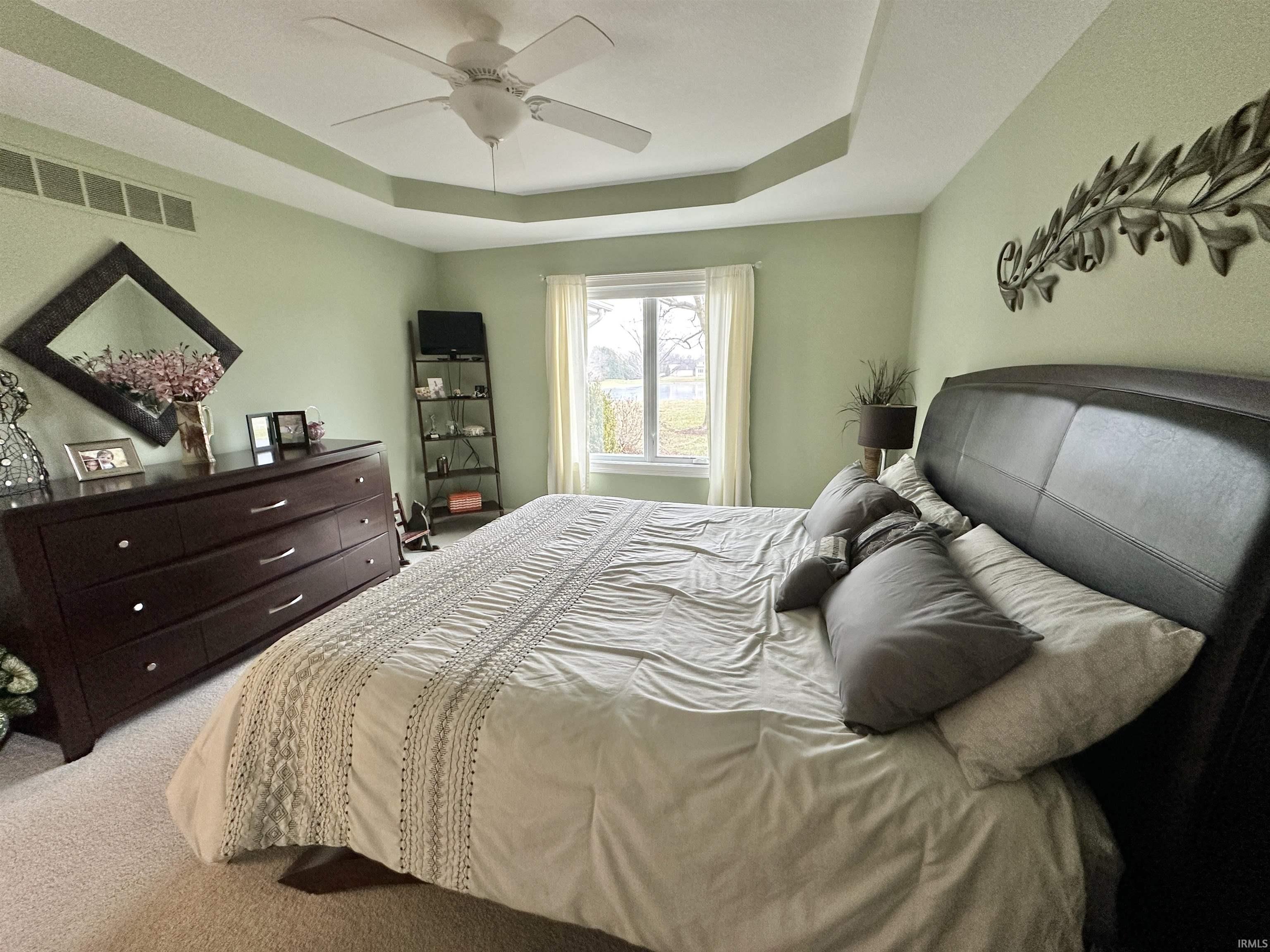 Carpeted bedroom with a tray ceiling and a ceiling fan