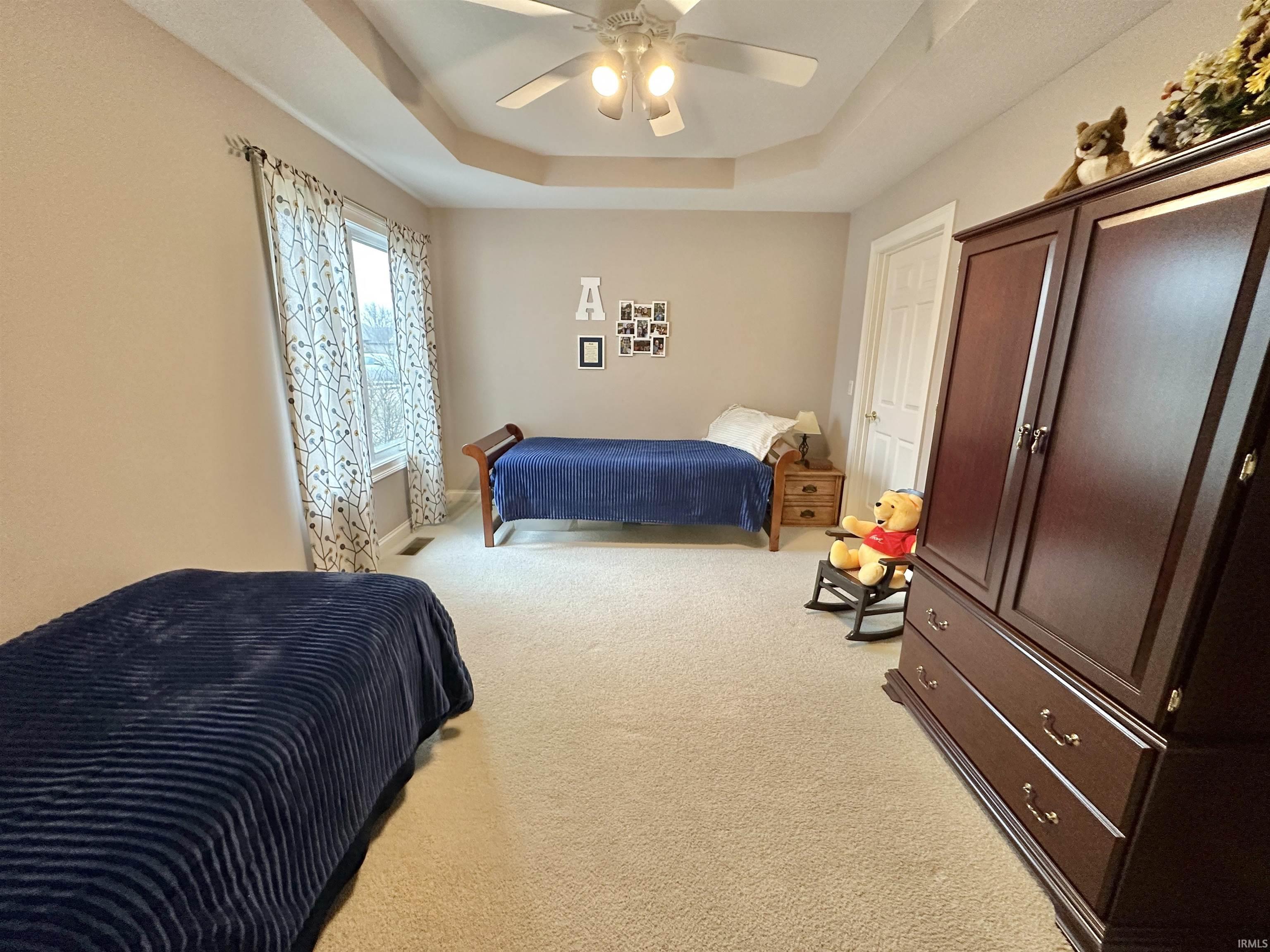 Bedroom with a tray ceiling, light colored carpet, and ceiling fan