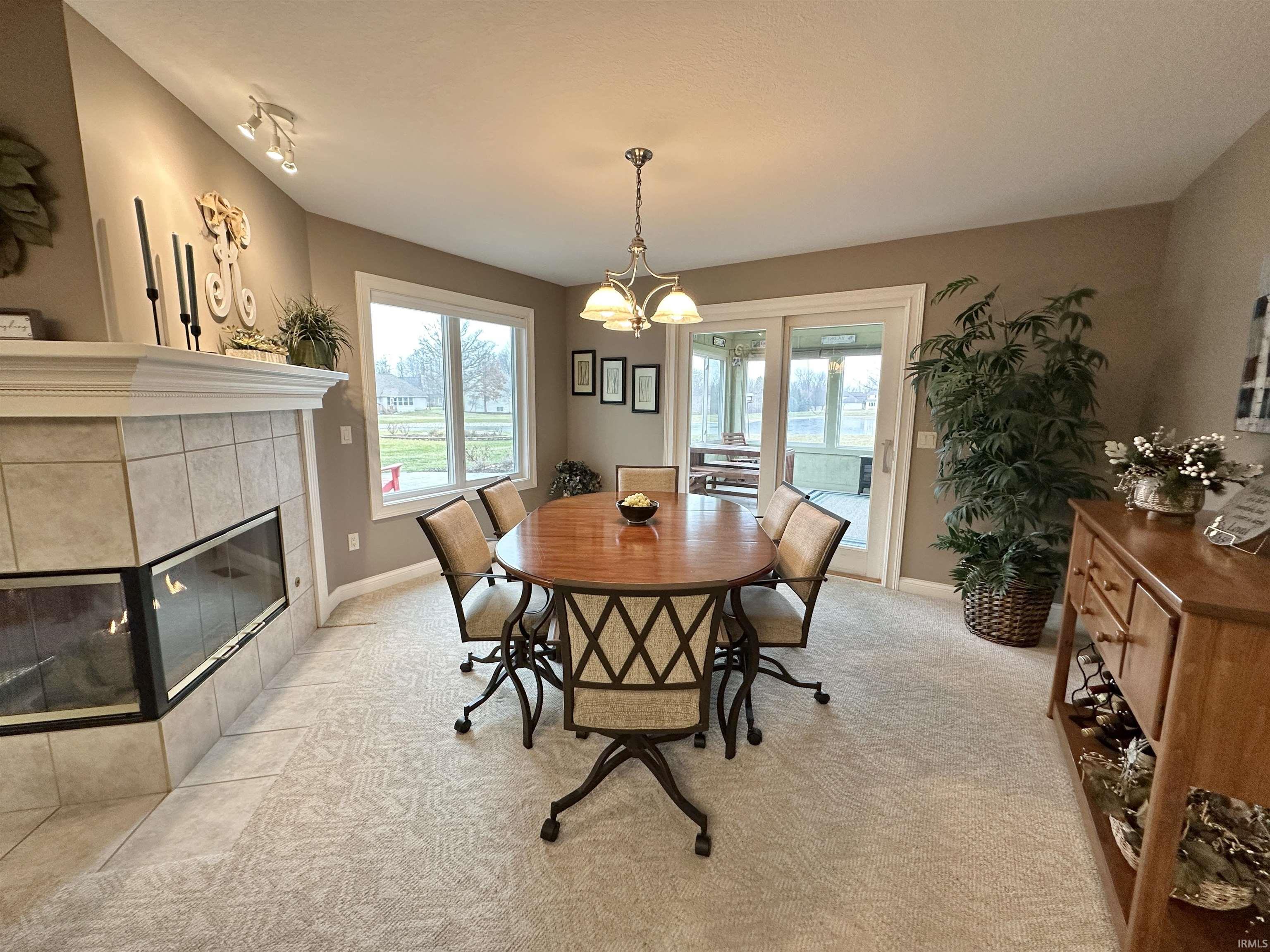 Dining room with light colored carpet, a tiled fireplace, and a chandelier