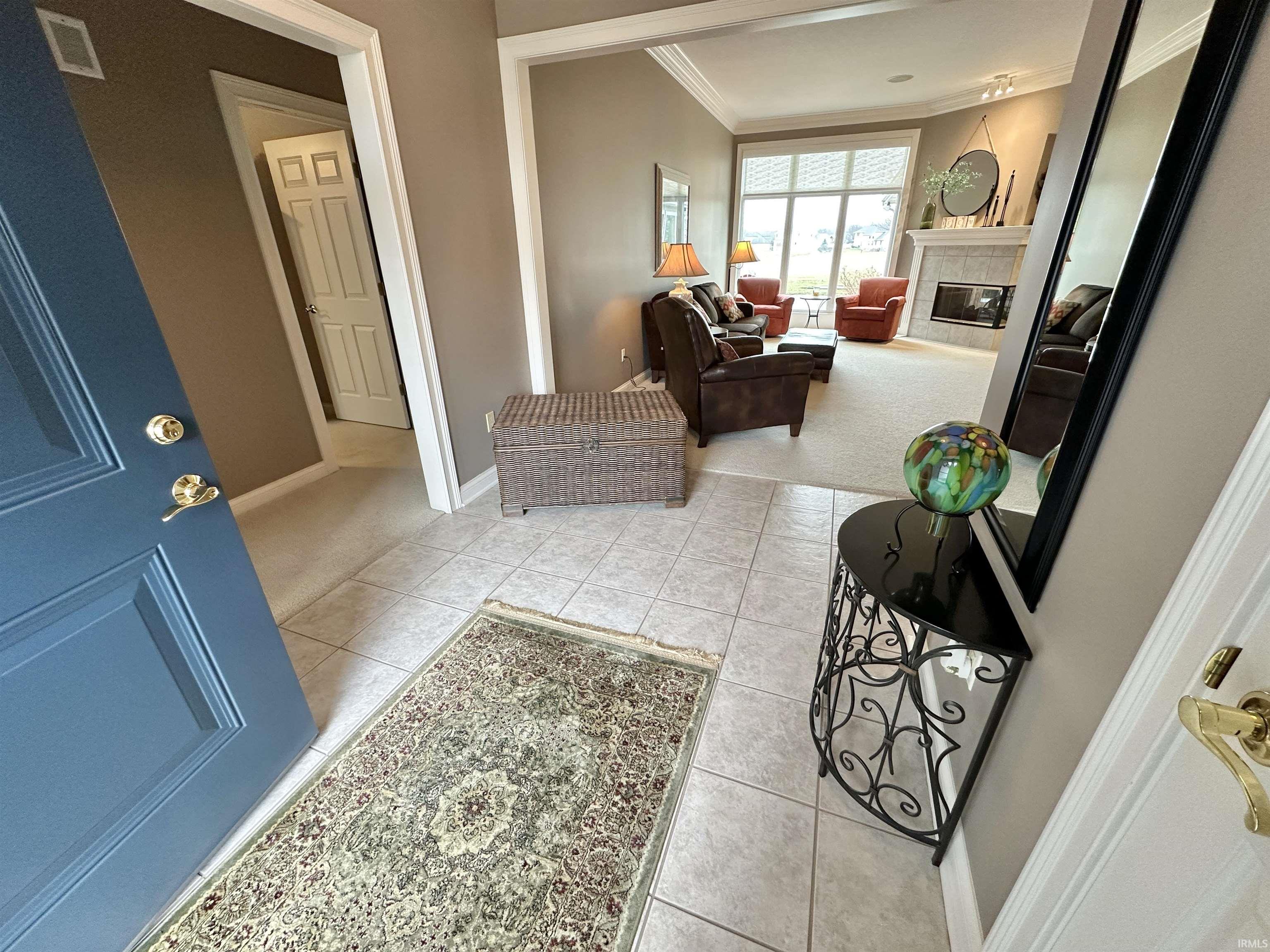 Entryway with light tile patterned floors, ornamental molding, a tiled fireplace, and light colored carpet