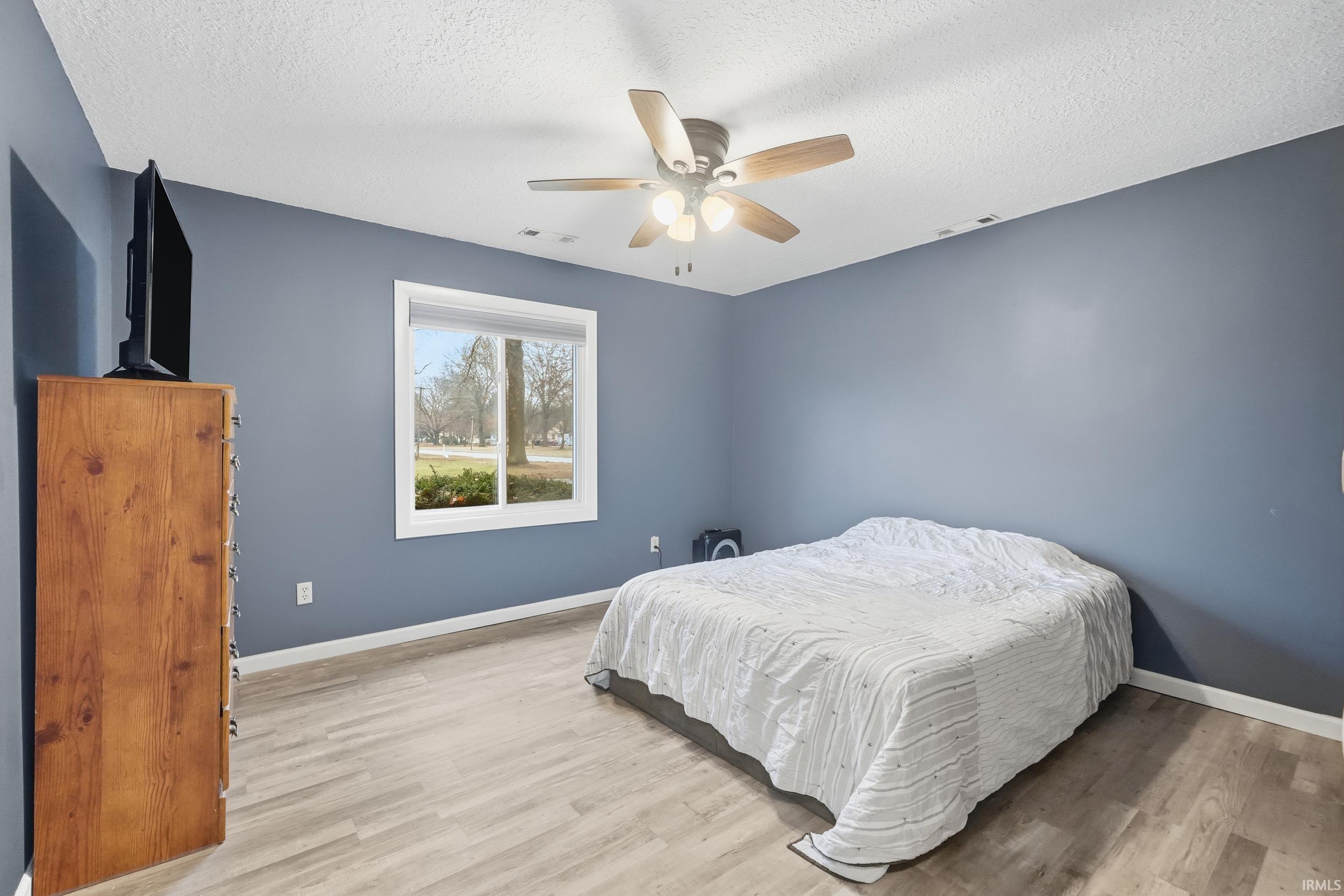 Bedroom with light wood-type flooring, a textured ceiling, and ceiling fan