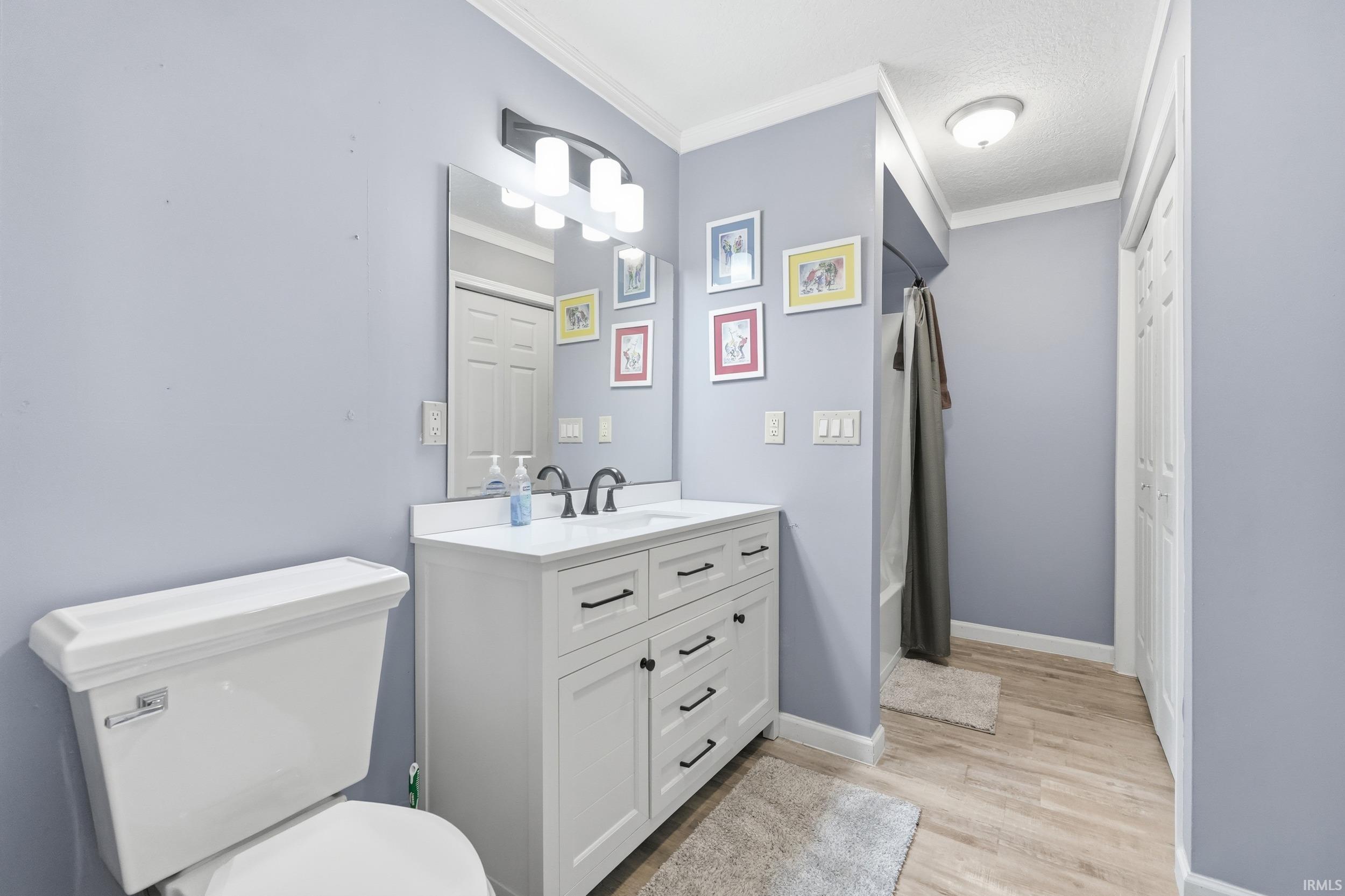 Full bath featuring vanity, crown molding, shower / bath combo, and light wood finished floors