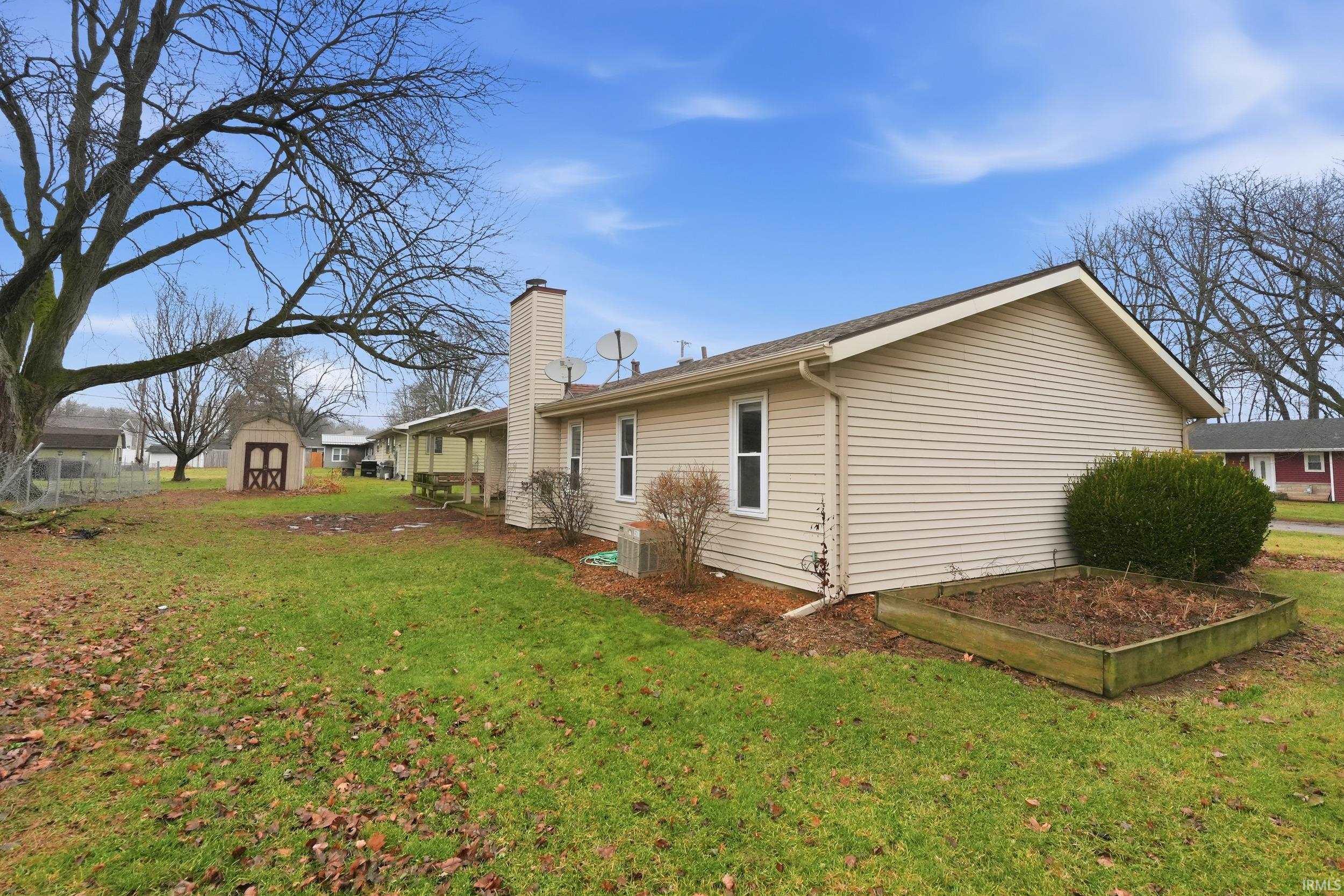 View of property exterior featuring a lawn, a chimney, a shed, and a vegetable garden
