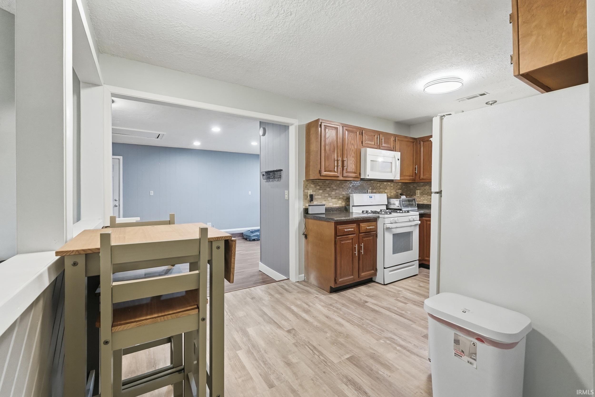 Kitchen featuring white appliances, dark countertops, brown cabinets, a textured ceiling, and light wood finished floors