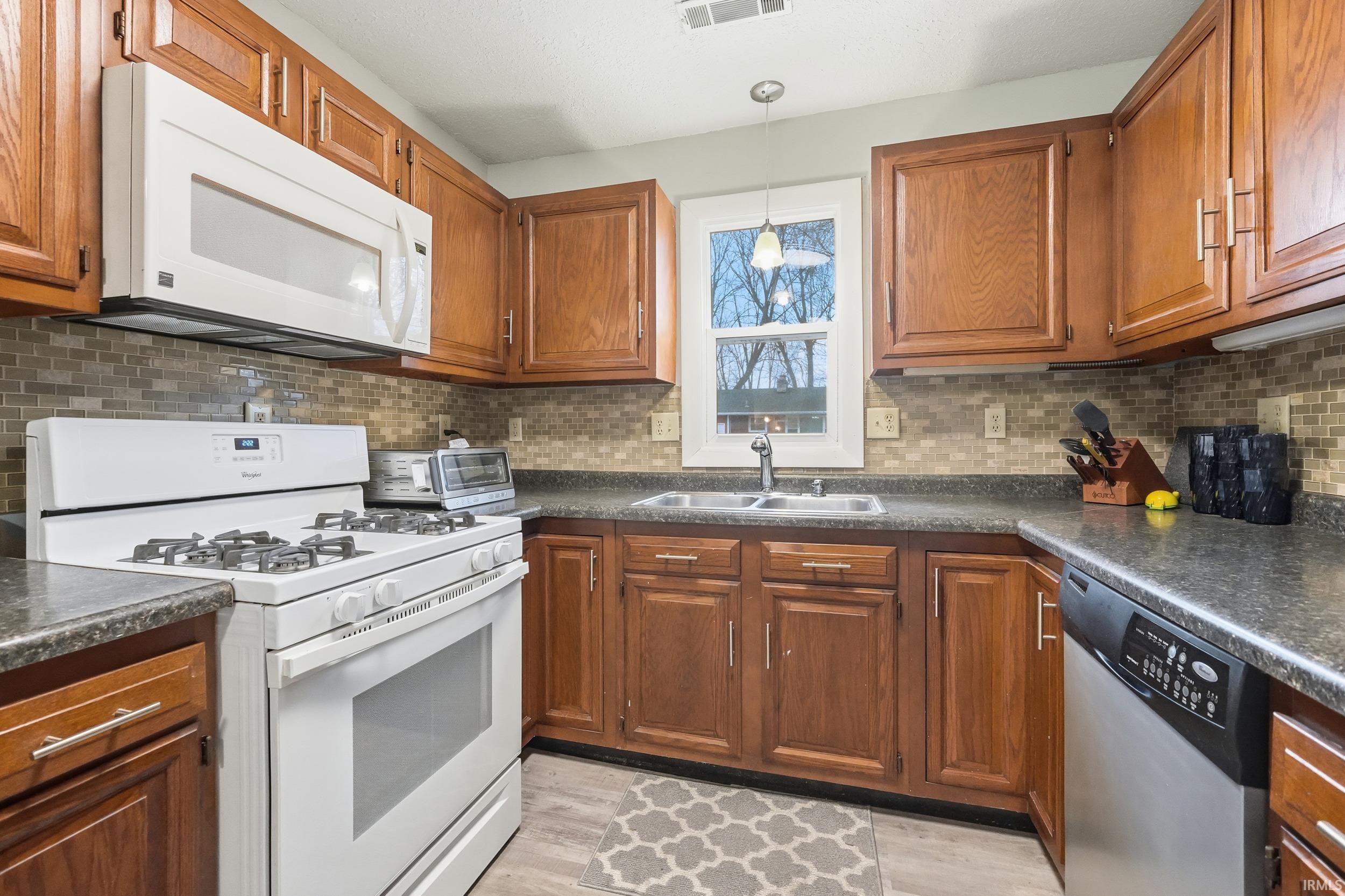 Kitchen featuring white appliances, dark countertops, and brown cabinetry