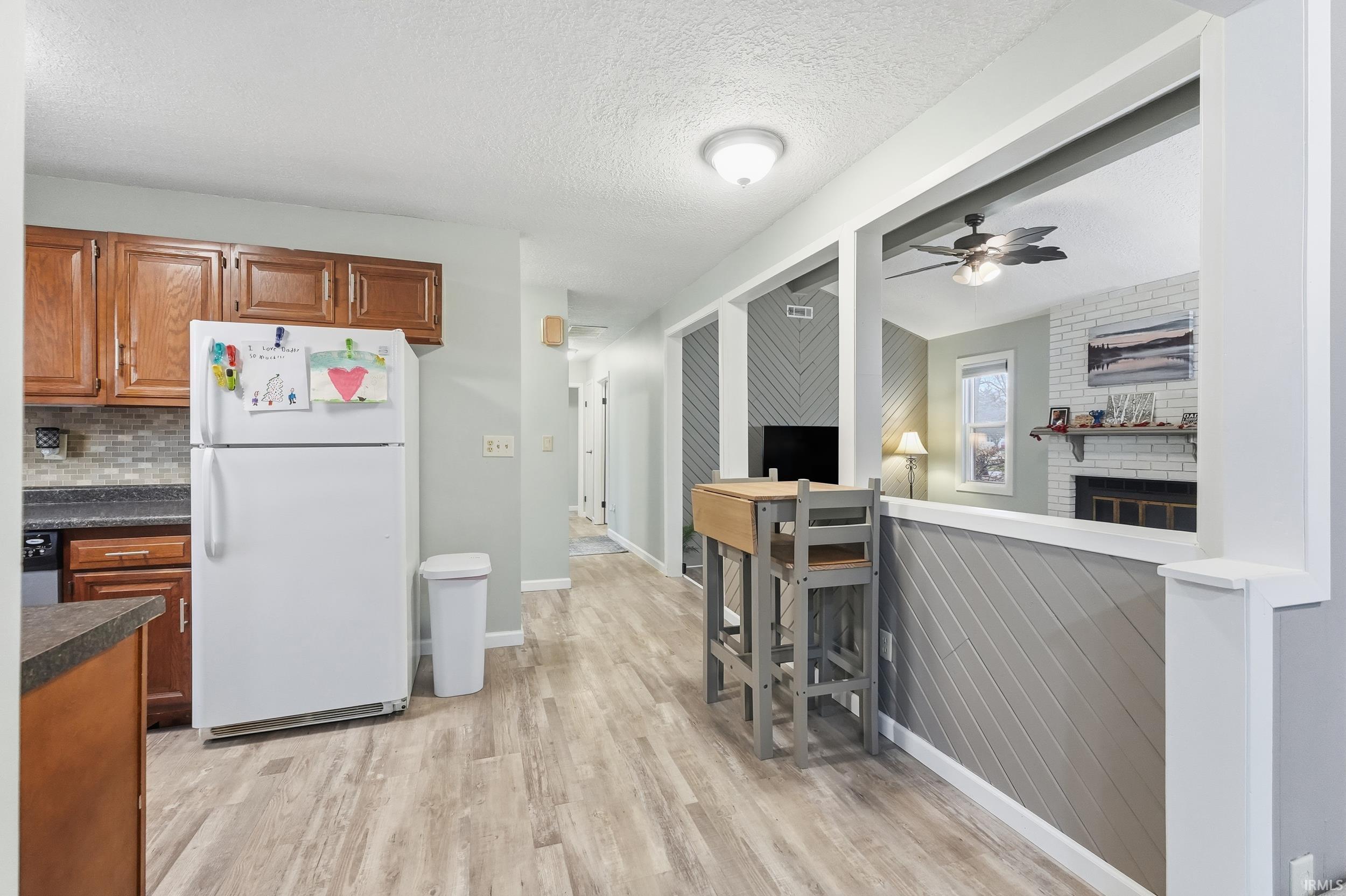 Kitchen with freestanding refrigerator, a textured ceiling, brown cabinets, dark countertops, and a ceiling fan