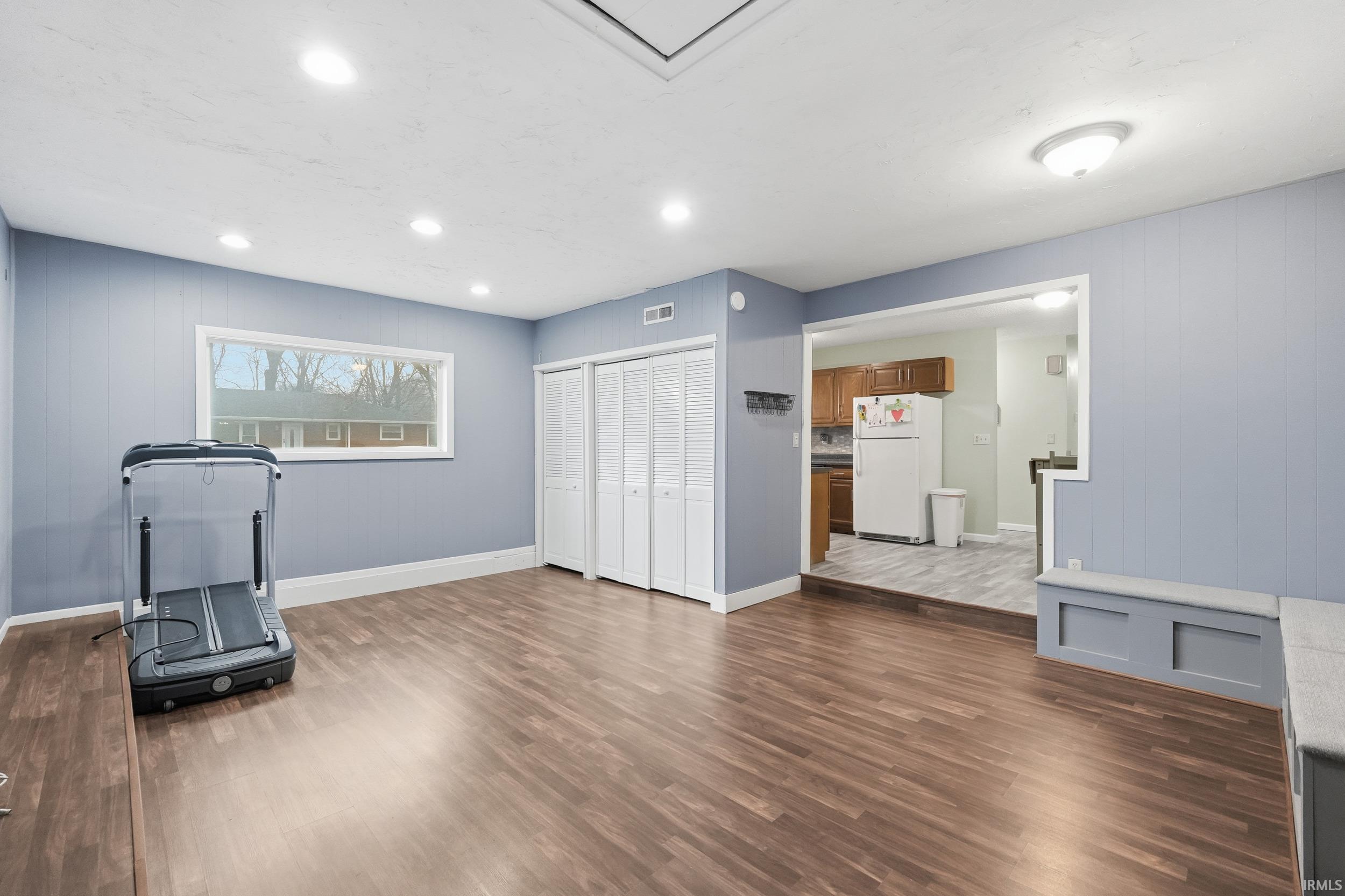 Workout area with dark wood-style flooring, wood walls, and recessed lighting