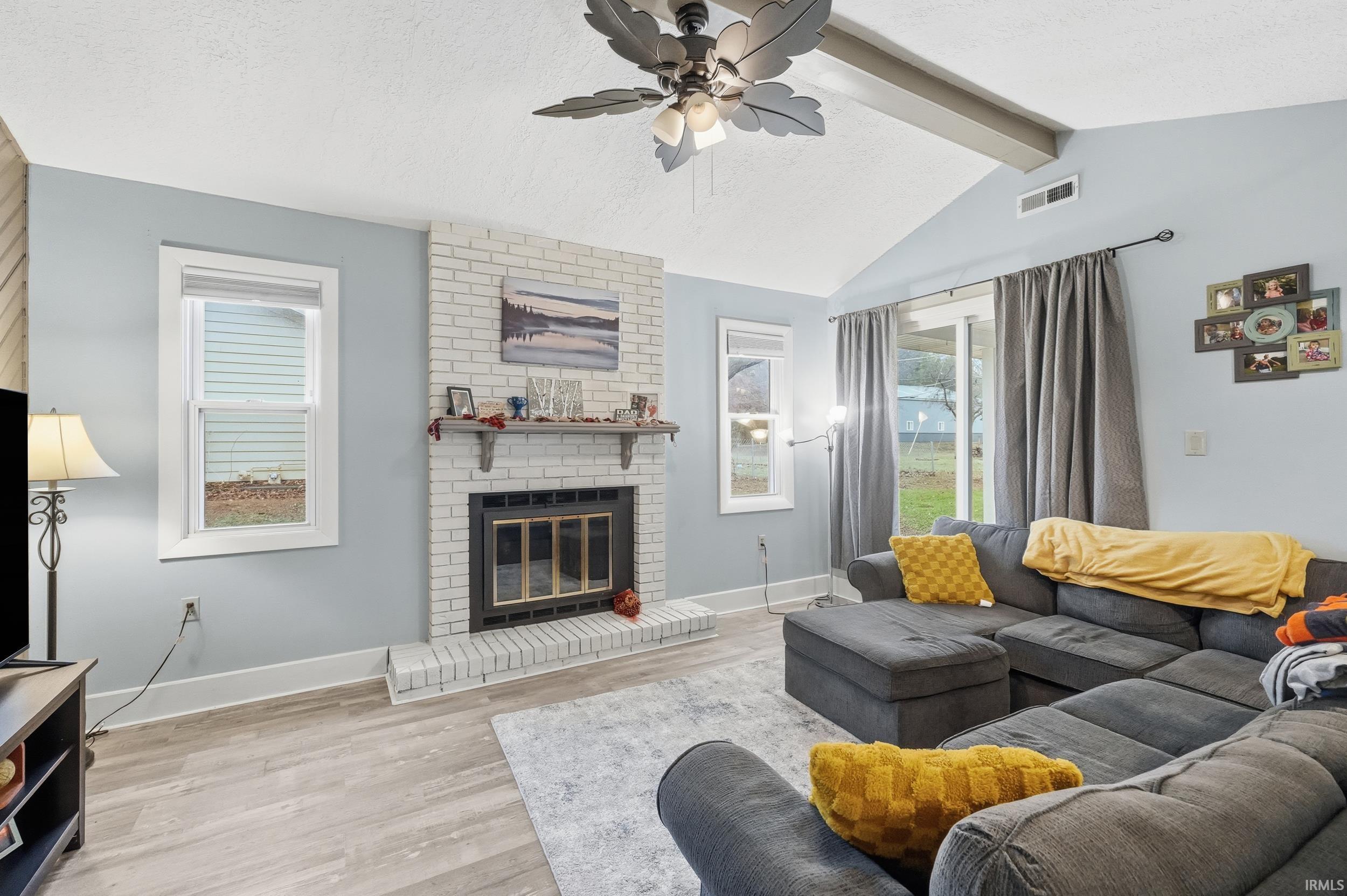 Living area with a textured ceiling, light wood-style flooring, a fireplace, and ceiling fan