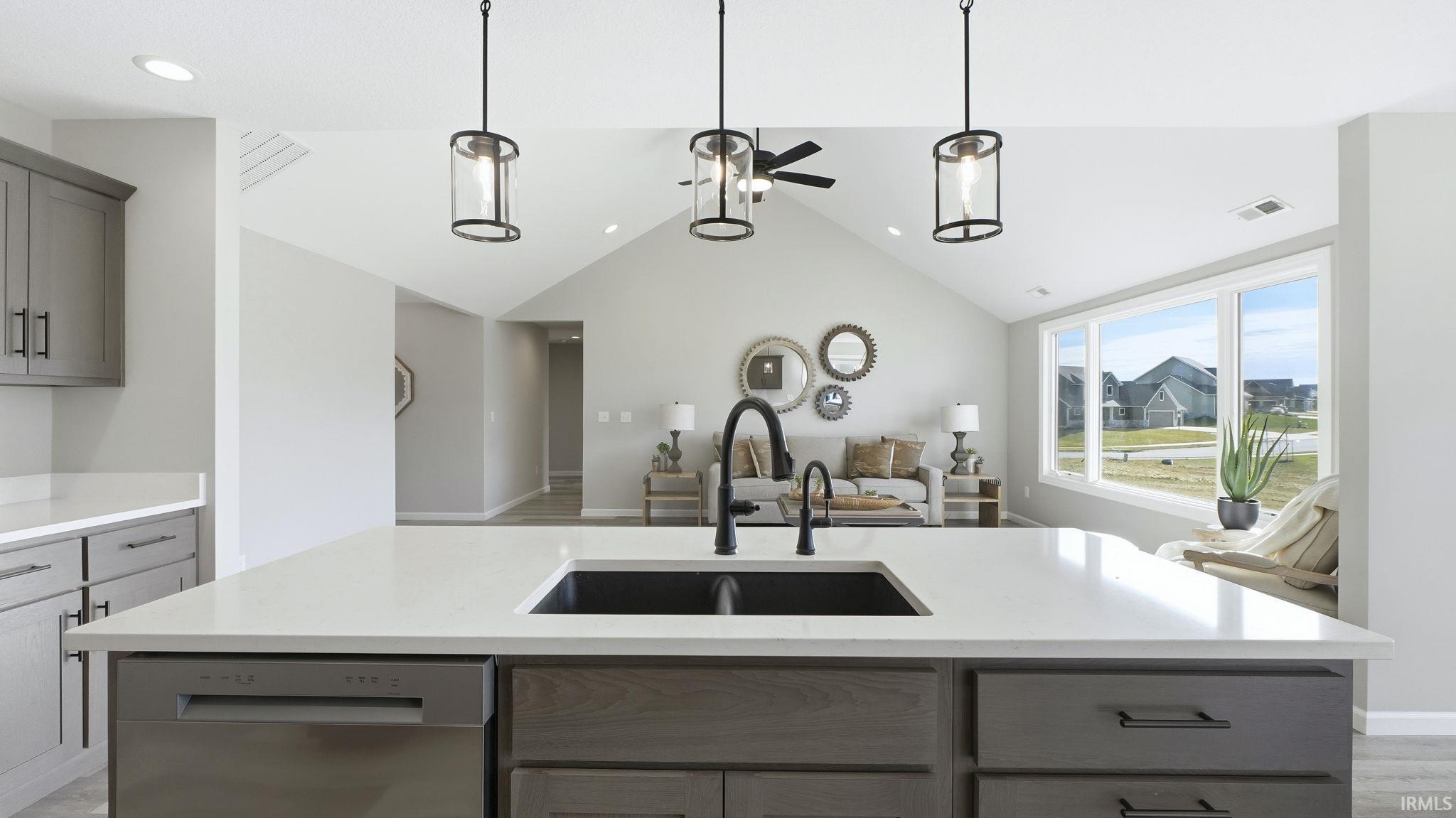 Kitchen with gray cabinets, stainless steel dishwasher, hanging light fixtures, a center island with sink, and vaulted ceiling