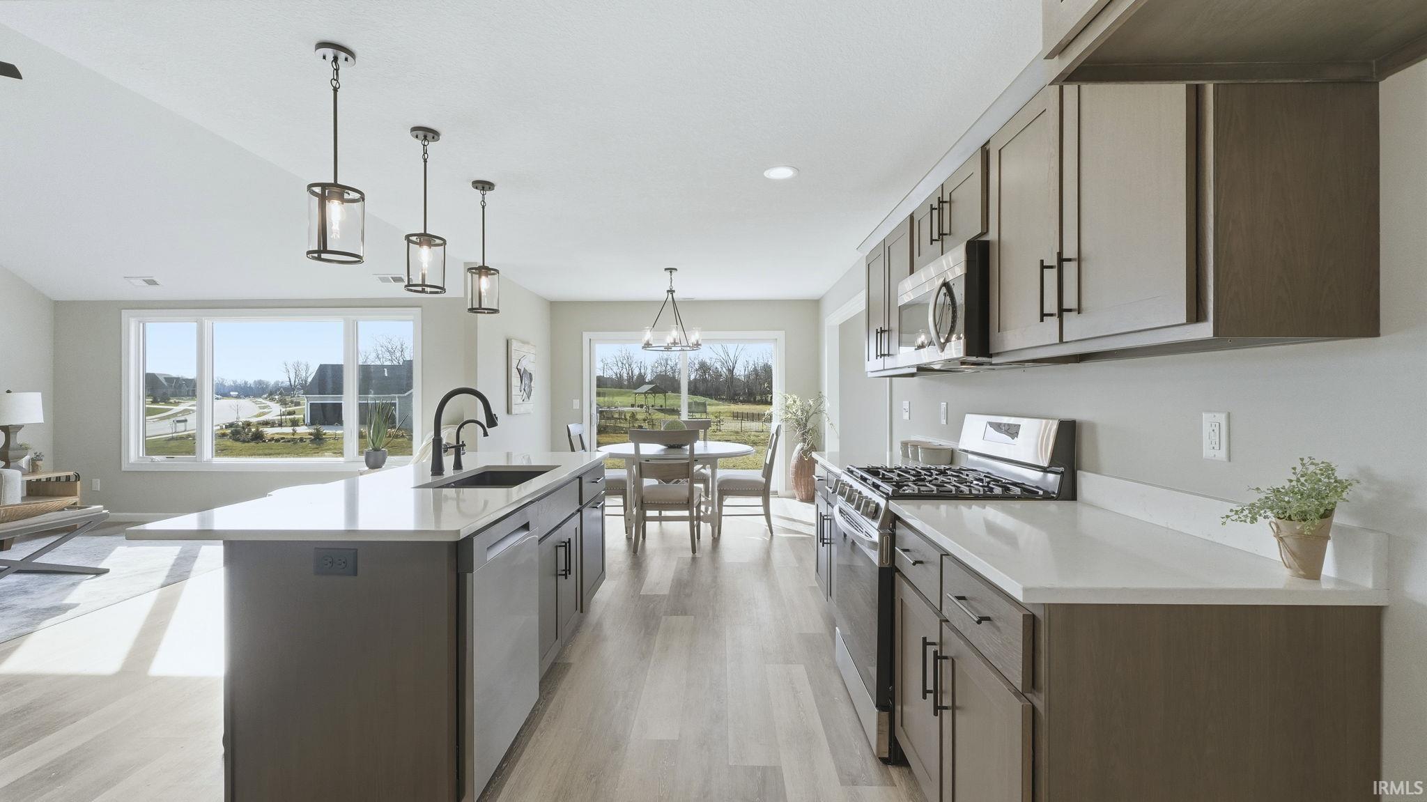 Kitchen with appliances with stainless steel finishes, hanging light fixtures, light wood-style floors, an island with sink, and dark brown cabinetry