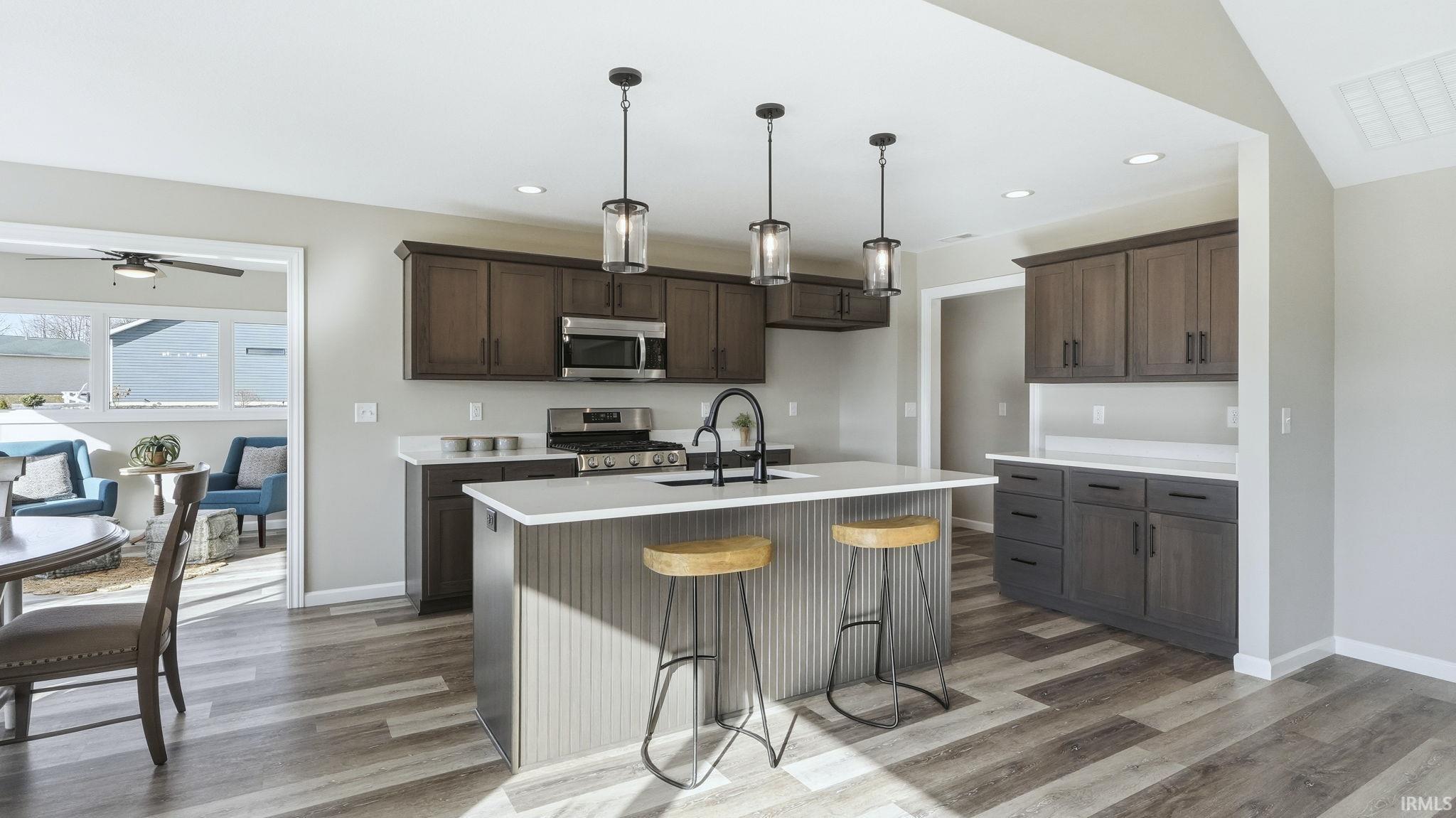 Kitchen with a kitchen breakfast bar, pendant lighting, appliances with stainless steel finishes, a kitchen island with sink, and dark brown cabinetry