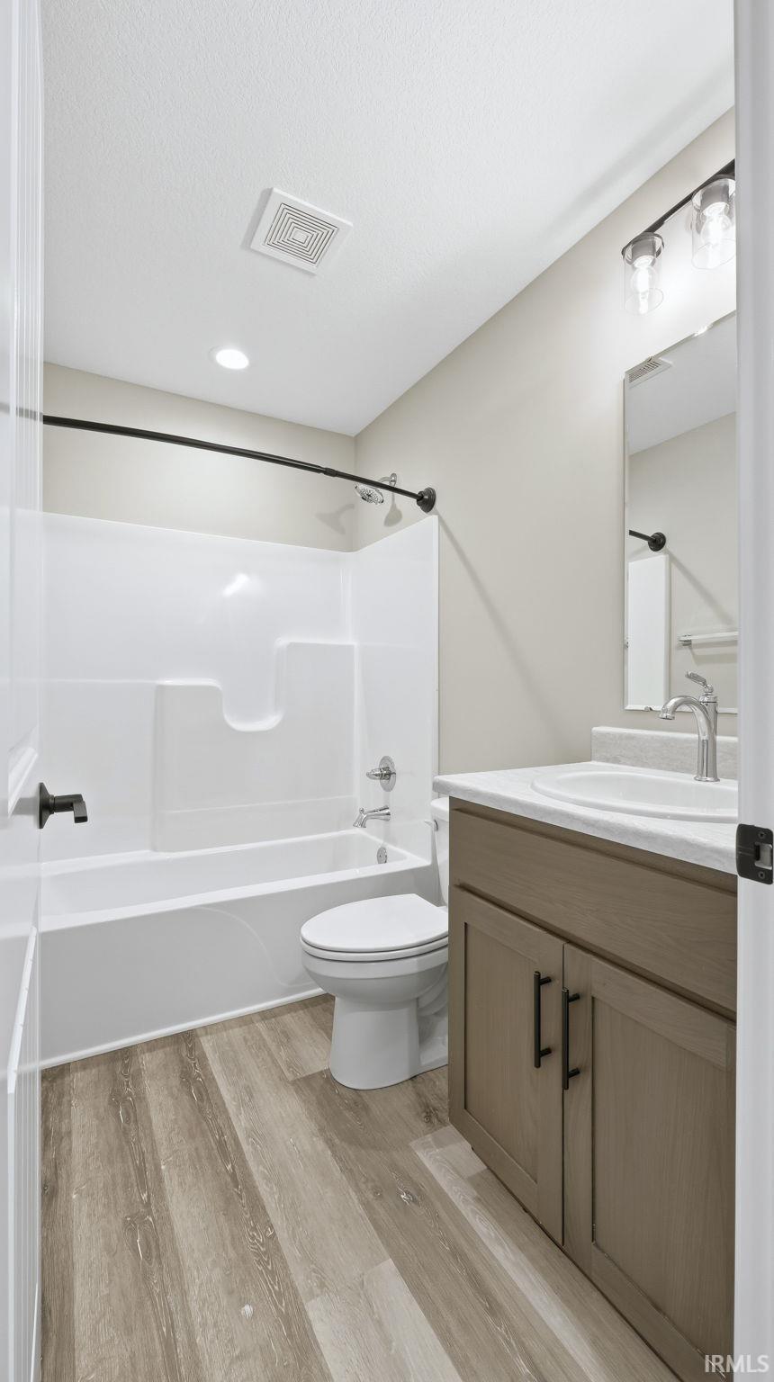 Full bathroom featuring vanity, shower / bath combination, light wood-style flooring, and a textured ceiling