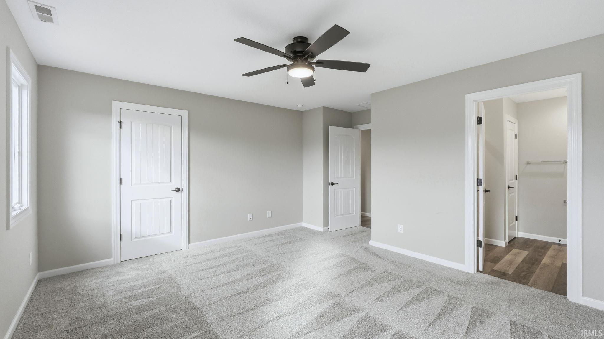Unfurnished bedroom with light colored carpet, a ceiling fan, and connected bathroom
