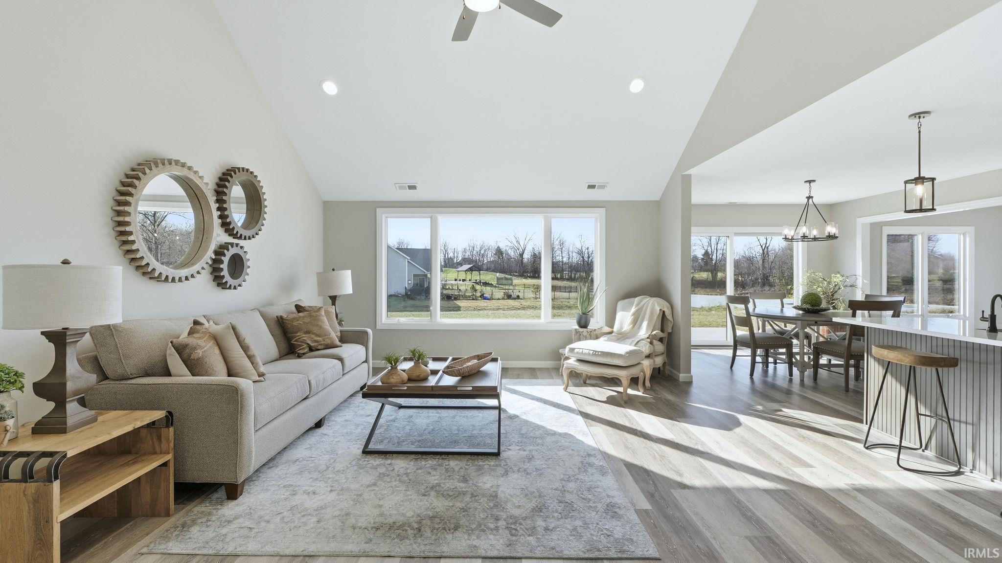 Living area featuring healthy amount of natural light, a chandelier, light wood finished floors, high vaulted ceiling, and a ceiling fan